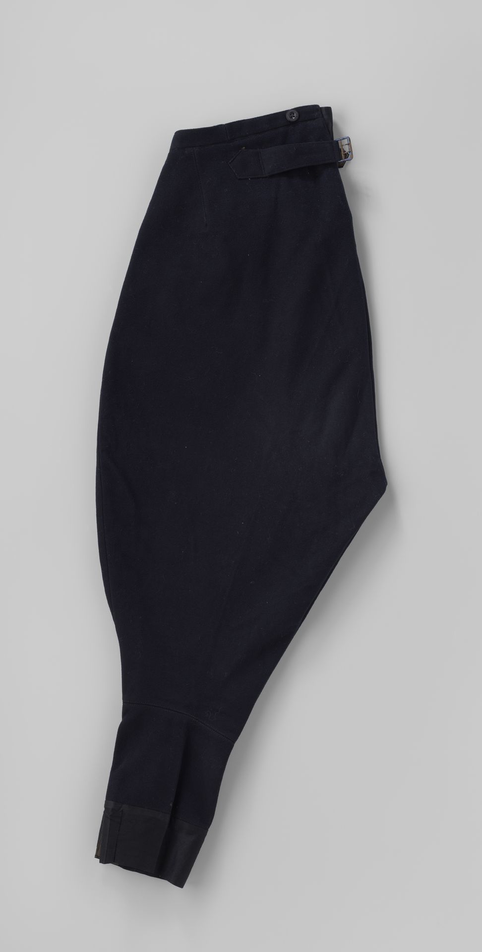 Poffende kuitbroek van zwart laken, met tailleband, hogere rug, gulp met blindsluiting, twee schuine zakken, één klepzak en vanachter banden met gesp; onderdeel chauffeurspak by Nieuw Engeland