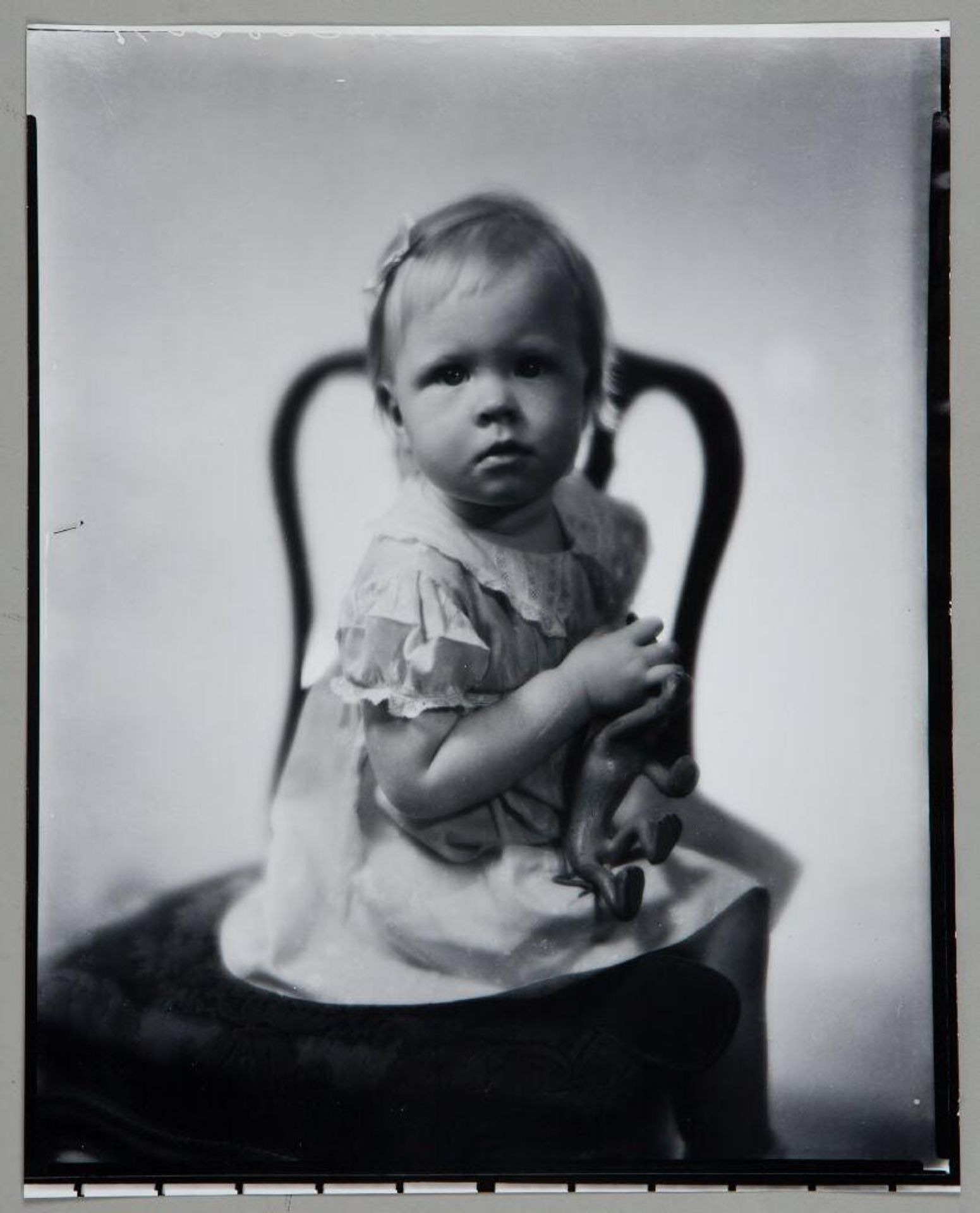 Untitled (small child seated on chair, holding animal toy) by Paul Gittings