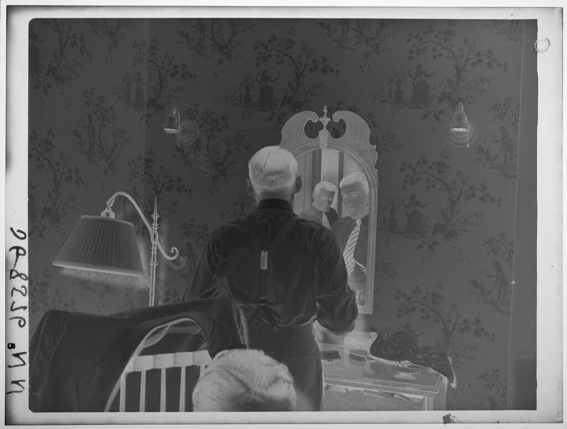 Untitled (two men reflected in mirror in room with dresser, lamp, and wallpaper) by Paul Gittings