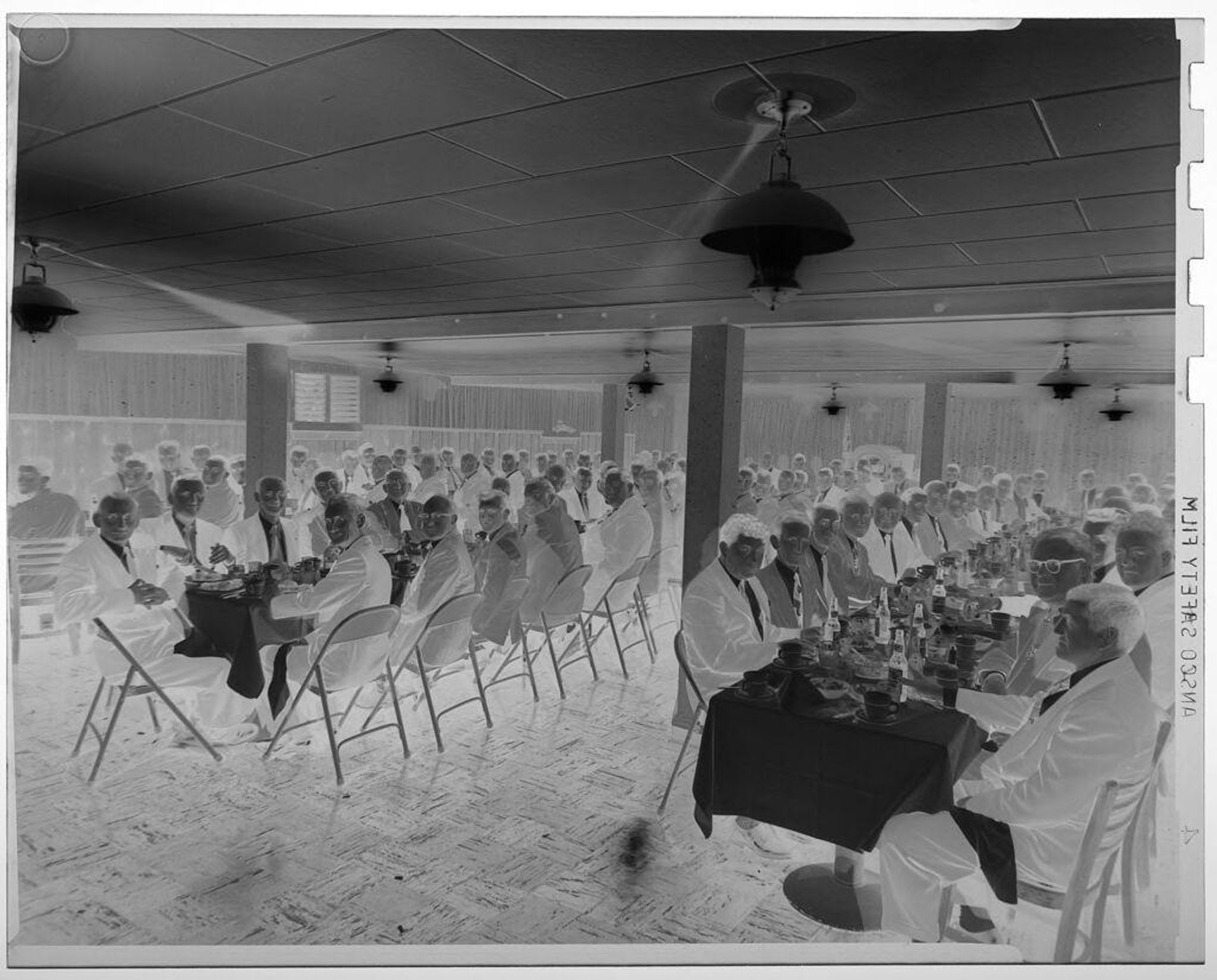 Untitled (large group of men eating and drinking at long banquet tables) by Jack Gould