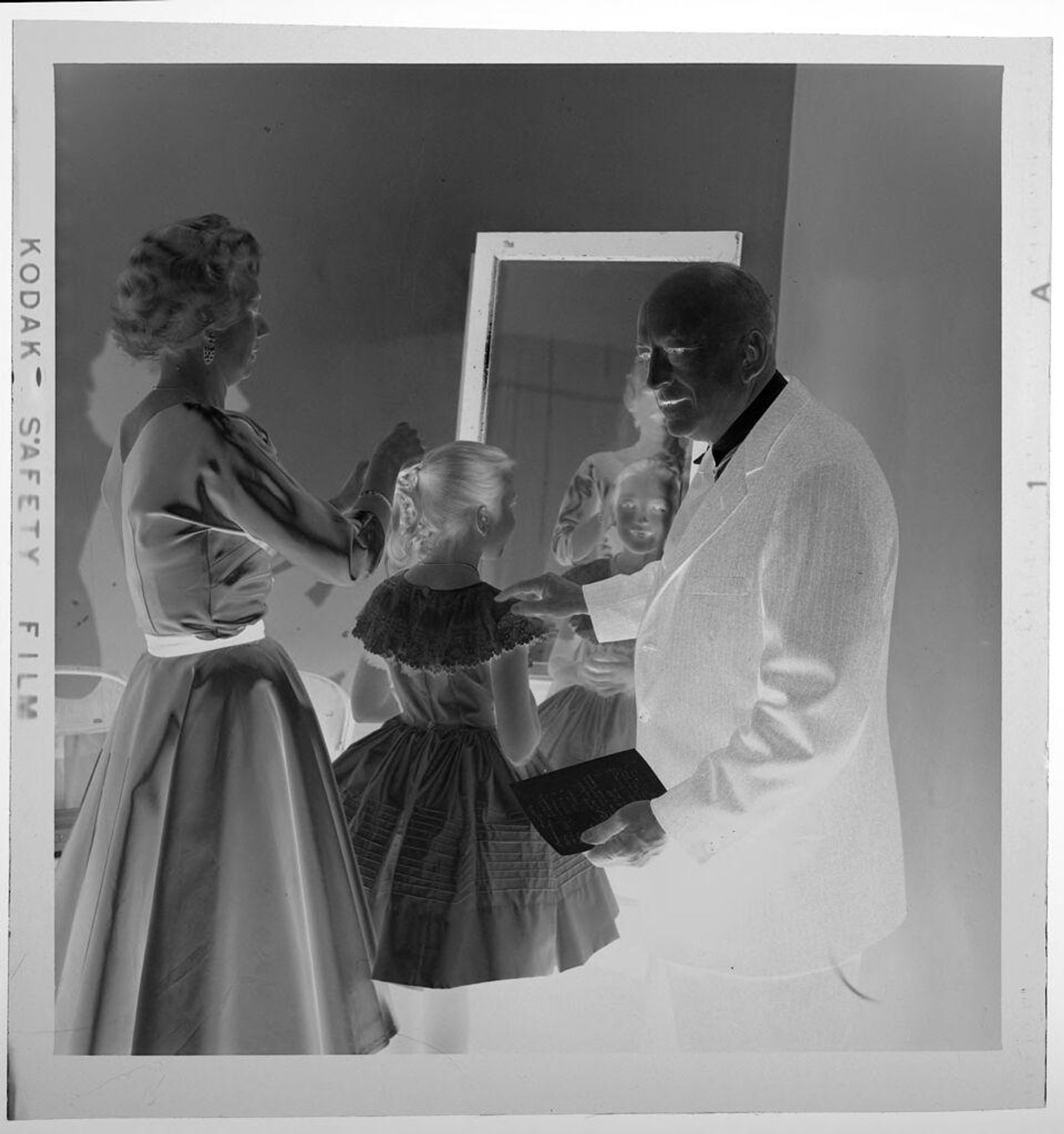 Untitled (woman fixing hair of girl in fancy dress, standing next to man in suit) by Jack Gould
