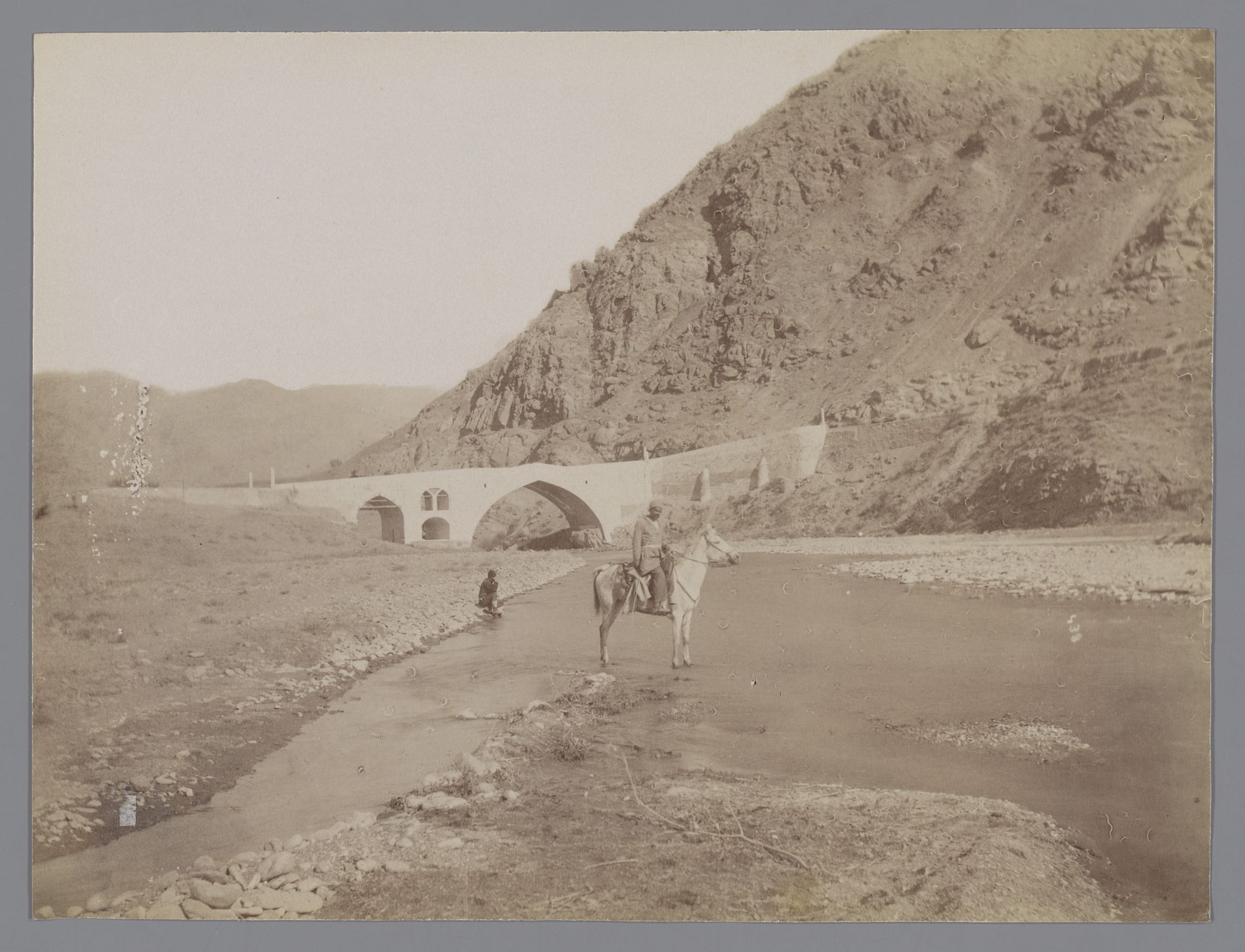 Landschap met een brug en een rivier met daarin een ruiter te paard en heuvels aan weerszijden ("La route de Rescht, Pont Kerezje [?]"), Iran by Antoine Sevruguin