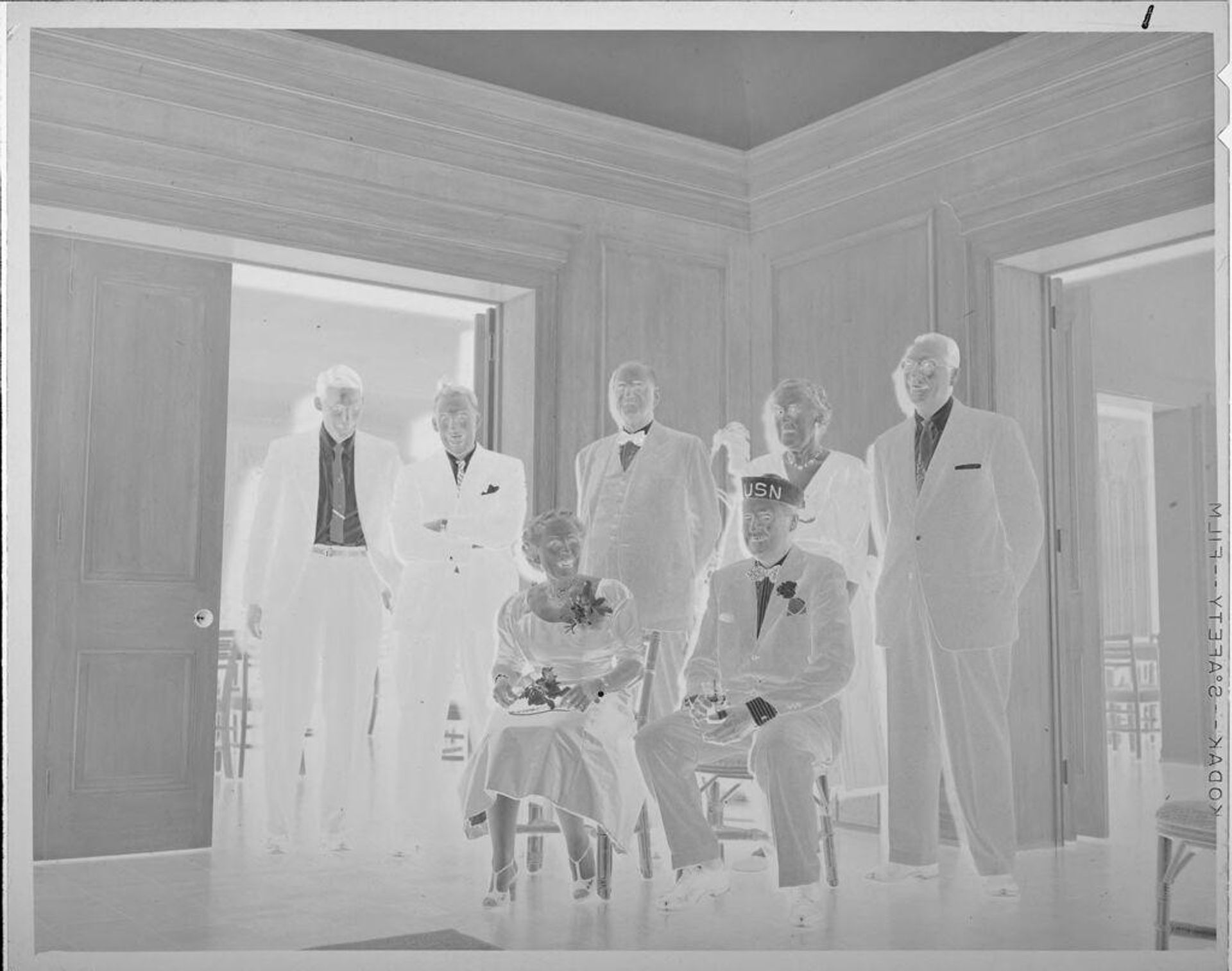 Untitled (man and woman on chairs, people standing behind) by Lucian and Mary Brown