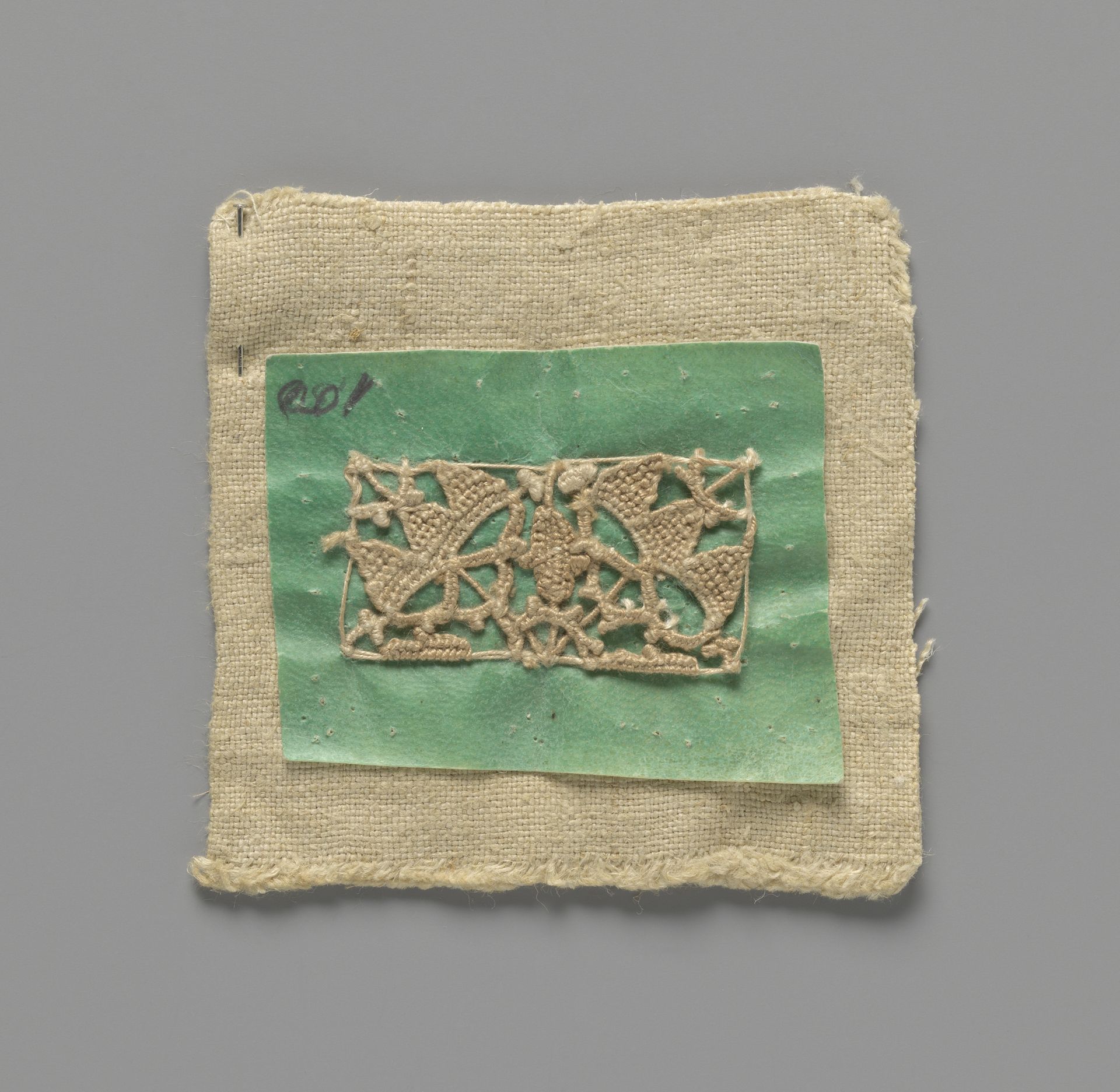Gereedschap voor een naaldkantmotief in de vorm van kleermakerslinnen waarop groen perkament is genaaid met een bijna voltooid motief in reticella-techniek met spandraden by Kantwerkschool (Den Haag)