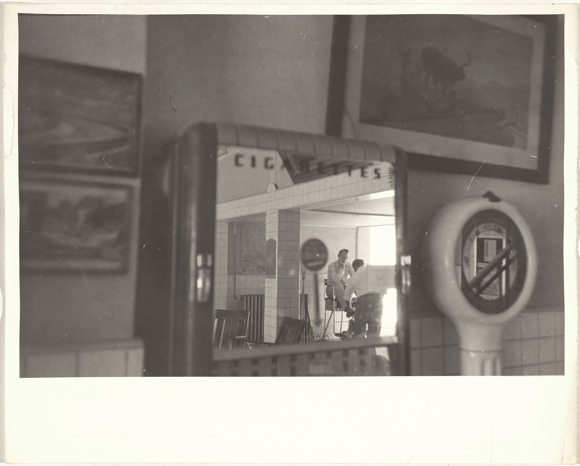 Shining shoes, reflection in cigarette machine mirror--New Mexico by Robert Frank