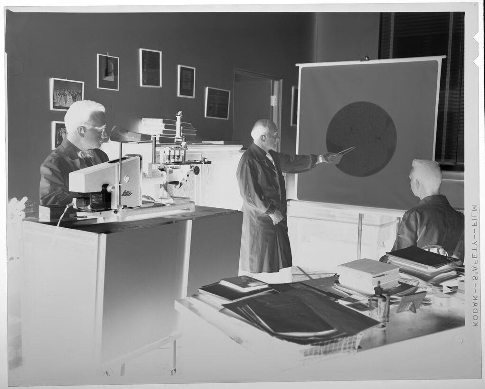 Untitled (scientist pointing at chart, two men watching) by Jack Gould