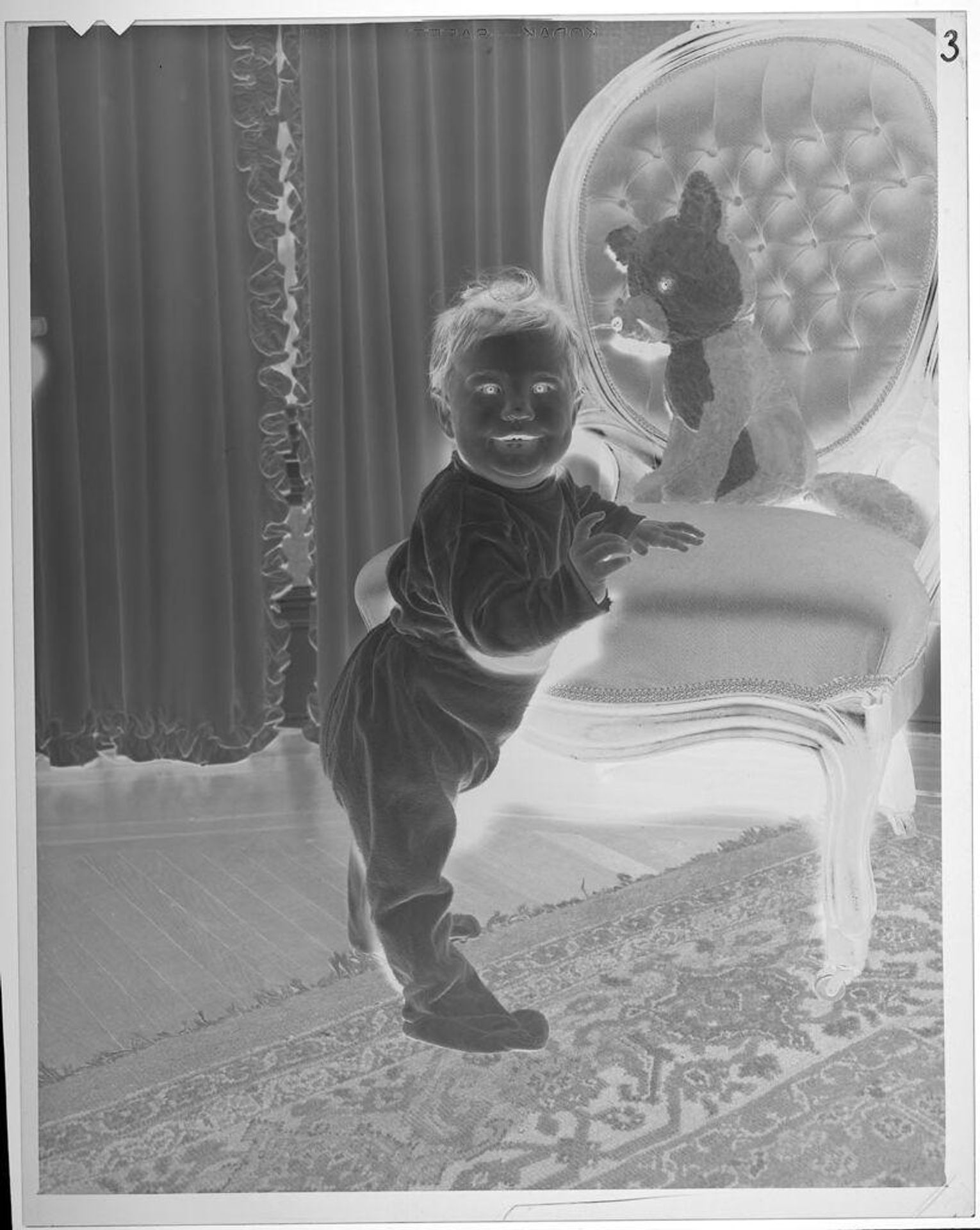 Untitled (baby standing next to chair, stuffed animal on chair) by Lucian and Mary Brown