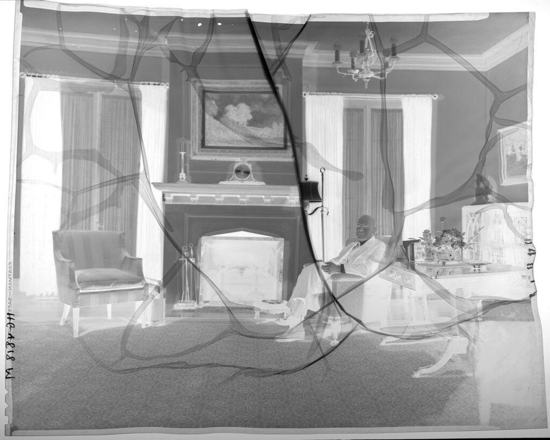 Untitled (man seated in armchair in living room between desk and fireplace) by Paul Gittings