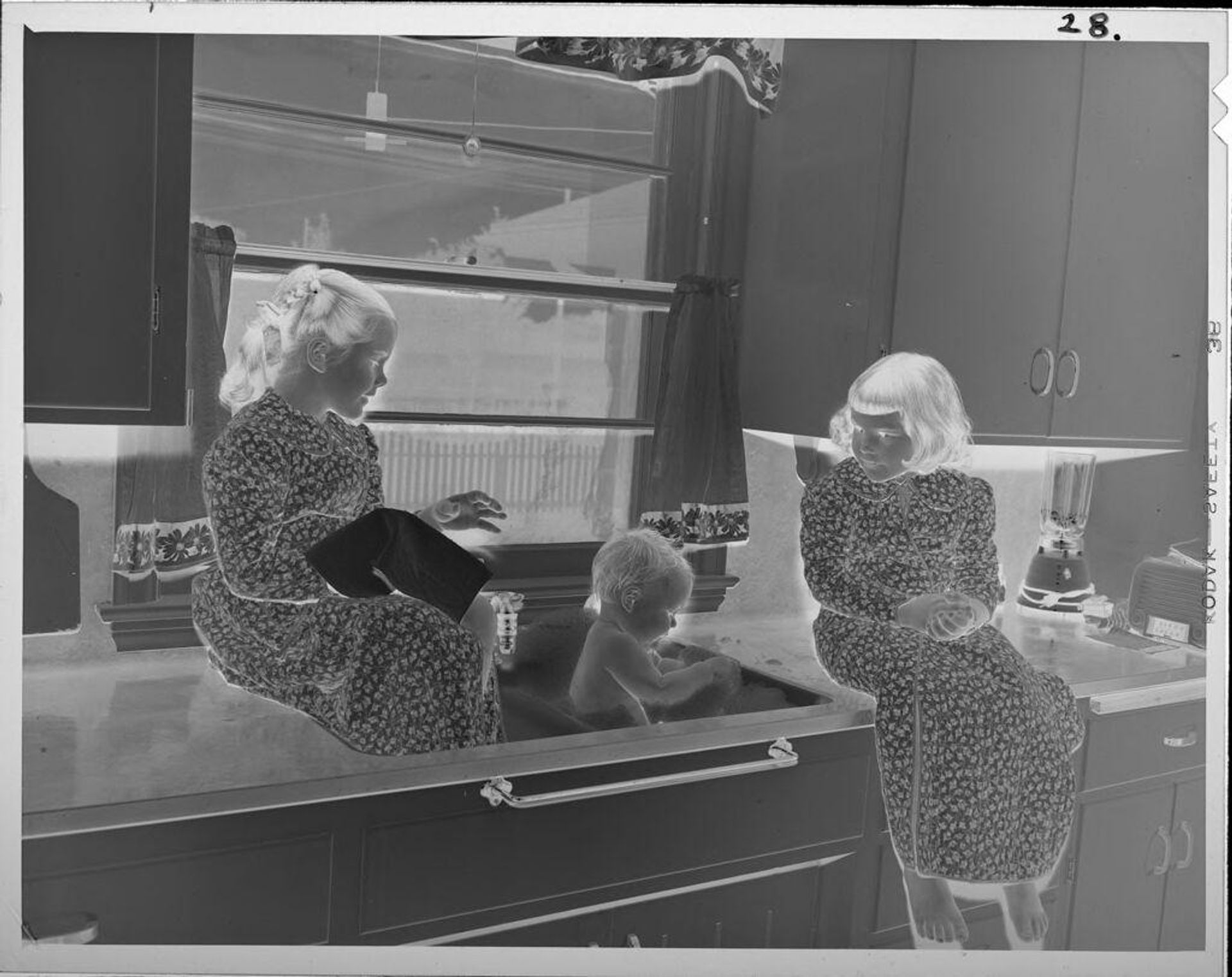 Untitled (girls giving baby a bath in sink) by Lucian and Mary Brown