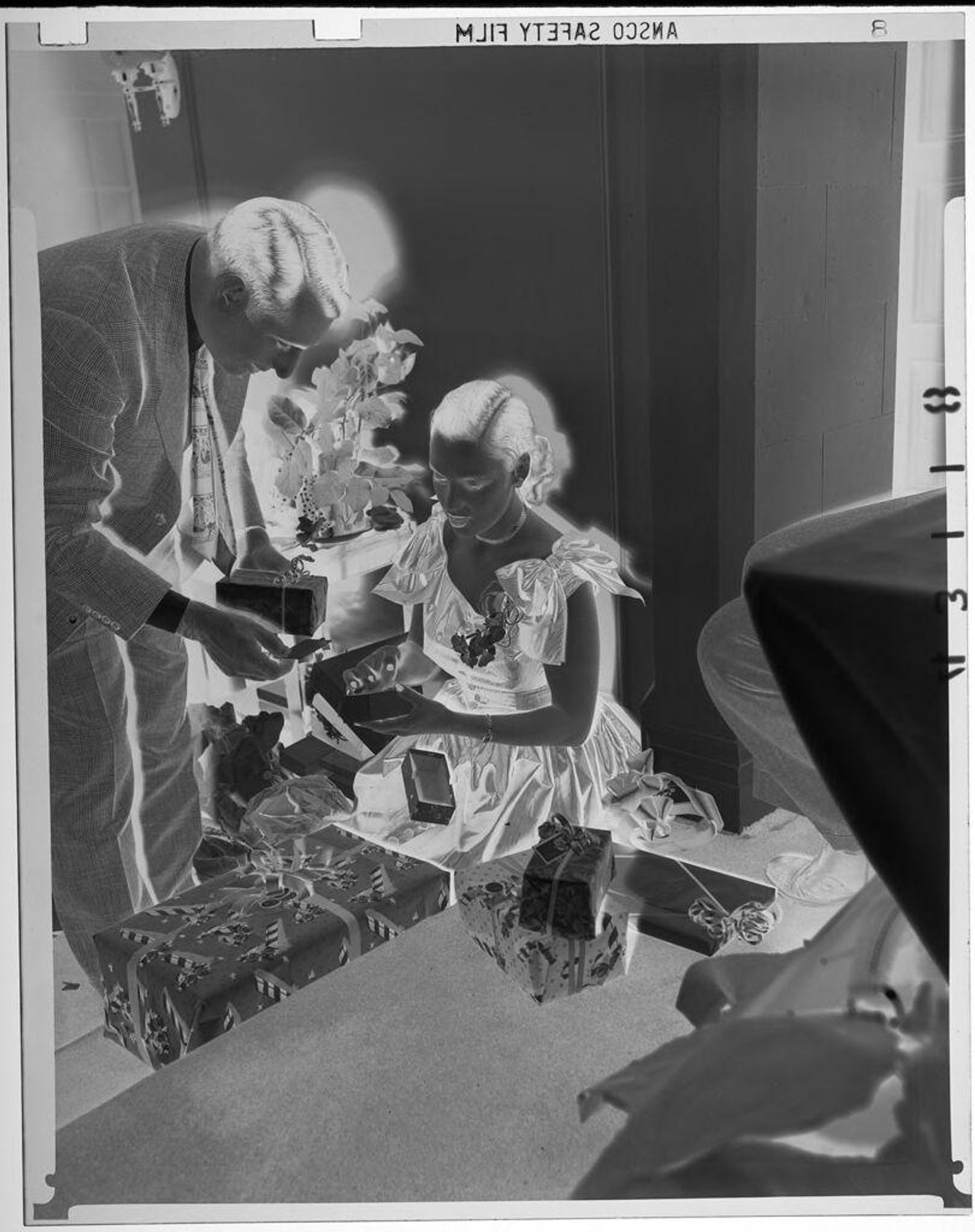 Untitled (young woman opening small gift box on floor as man examines gift and card beside her) by Martin Schweig