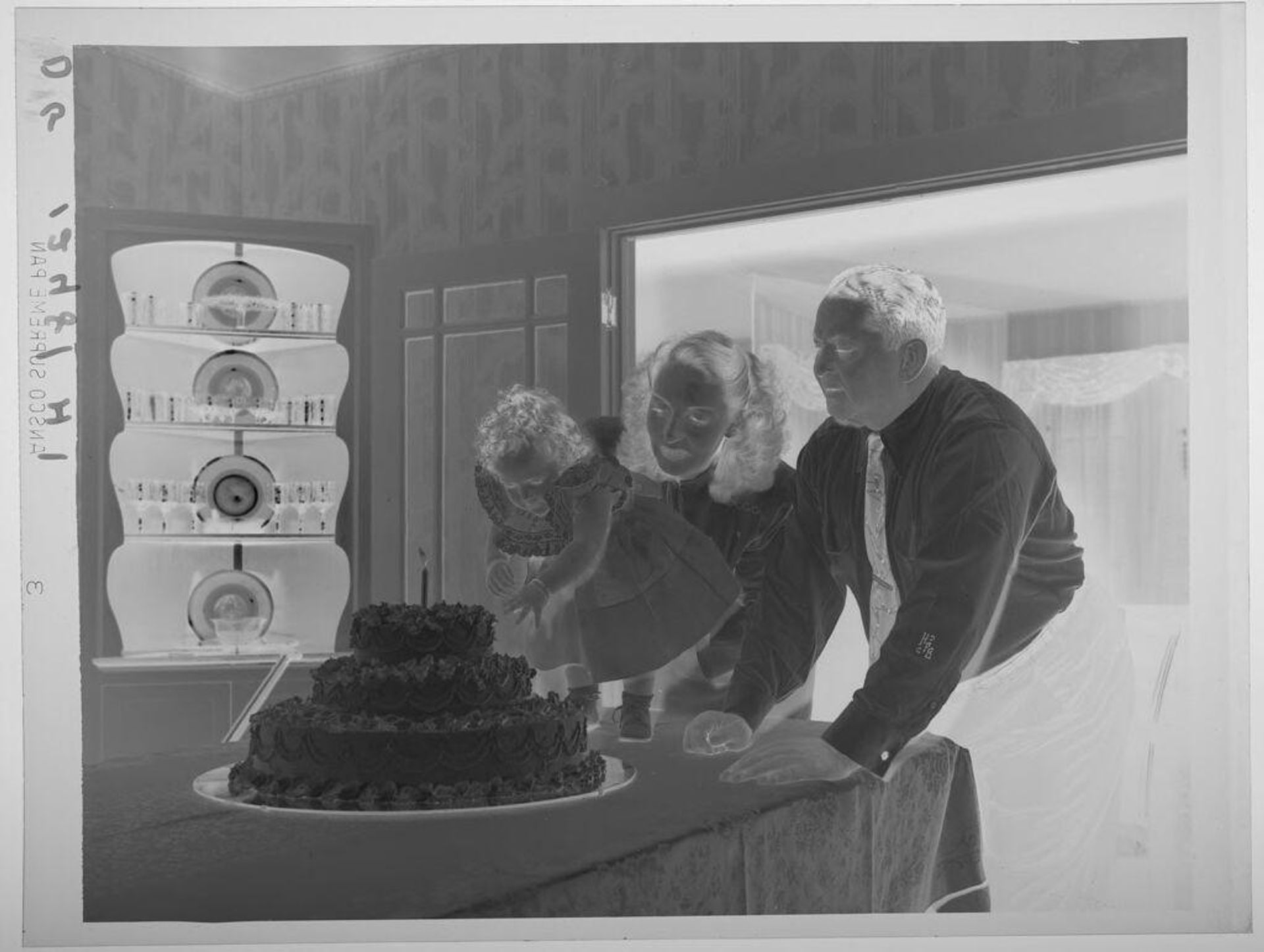 Untitled (little girl leaning over toward first birthday cake, parents behind her) by Paul Gittings