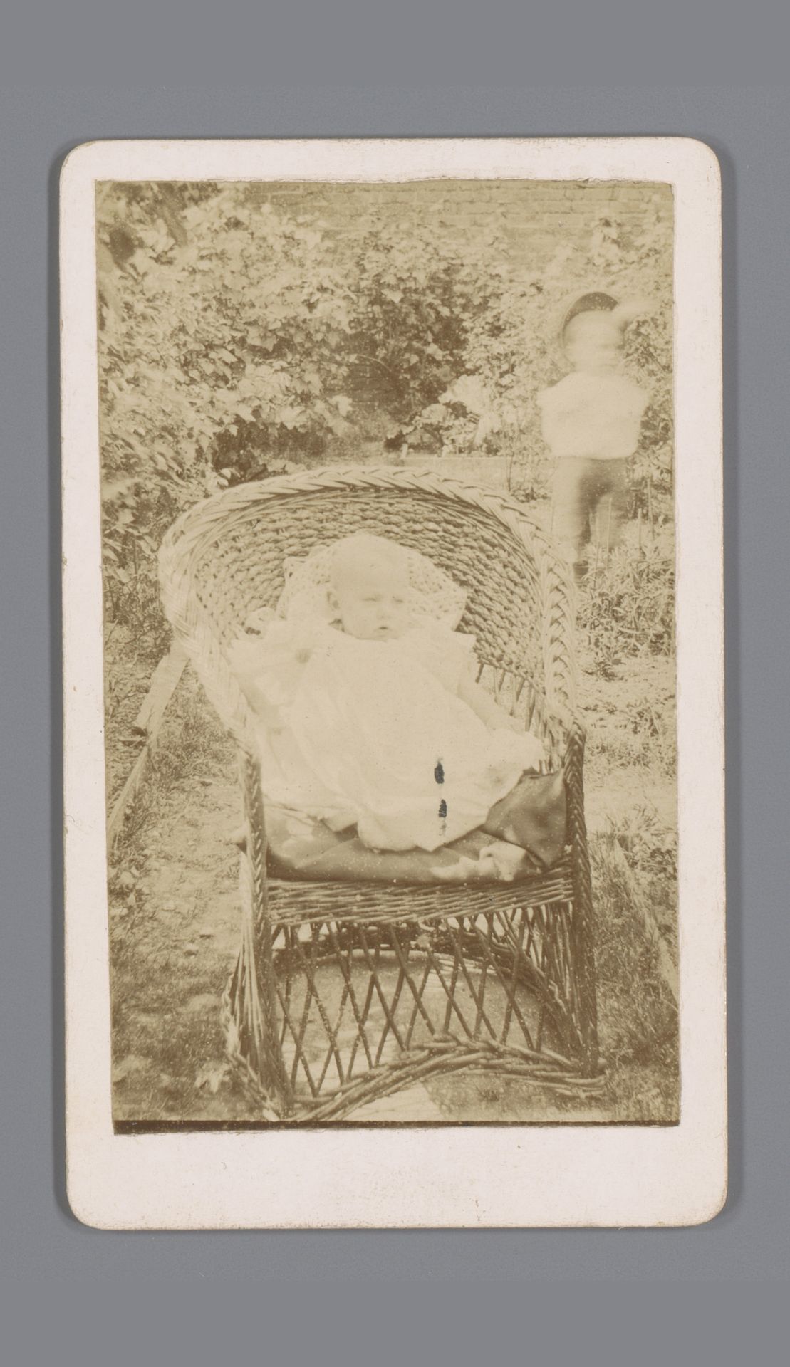 Portret van een onbekende baby in rieten stoel in een tuin by John George Kirby