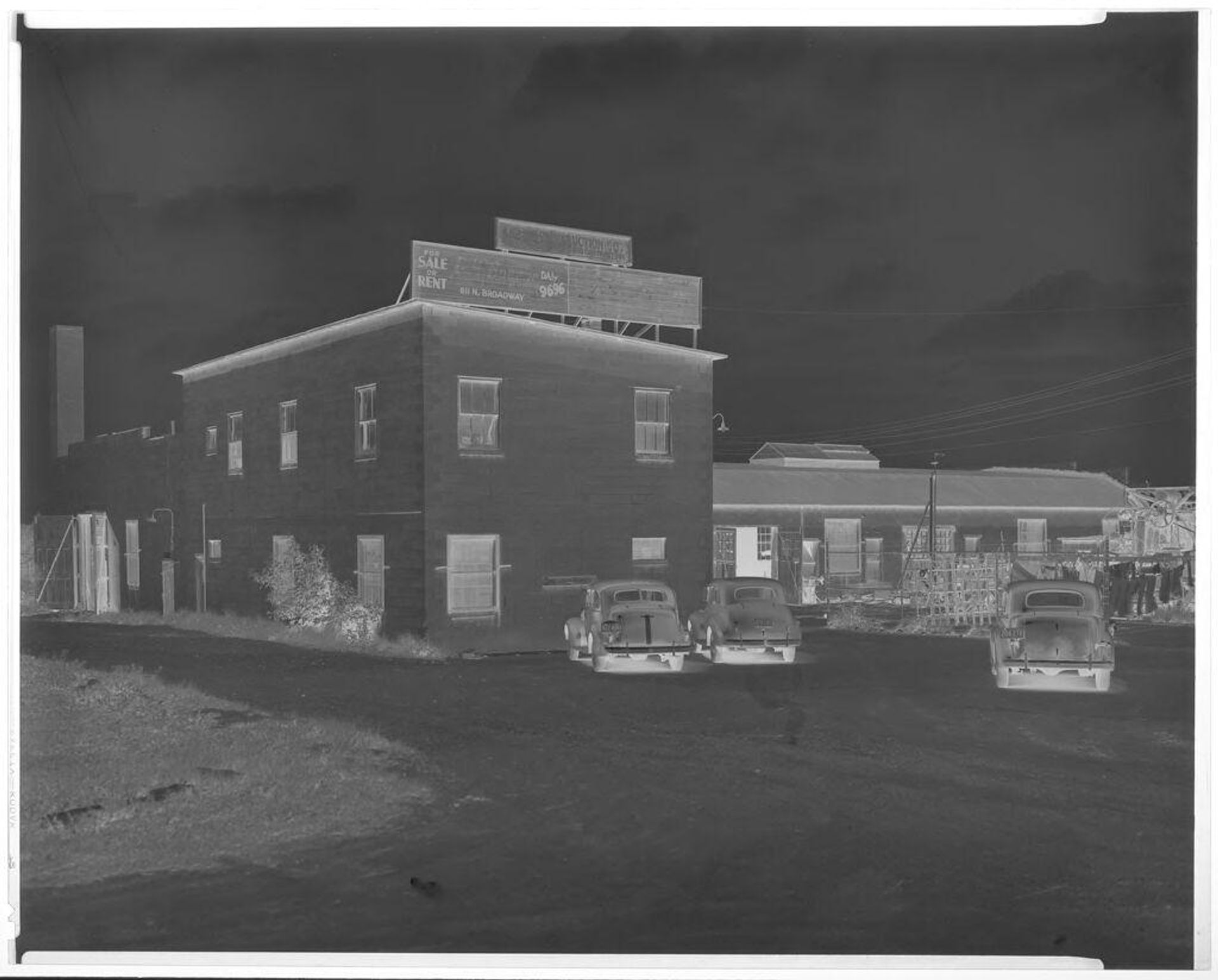 Untitled (exterior view of building with cars out front) by John Deusing