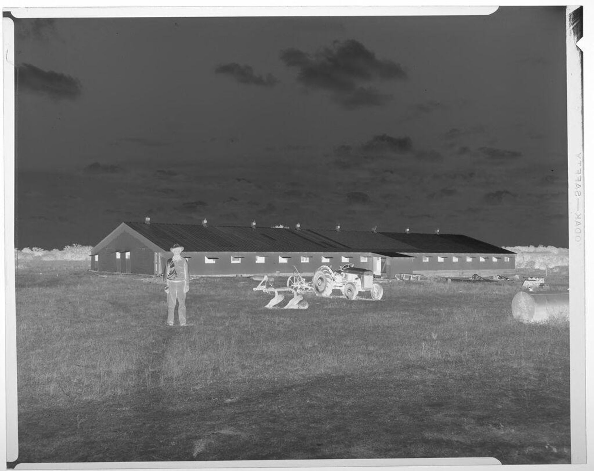 Untitled (man and tractor in field in front of buildings, Armo Mills Broiler operations) by Harry Annas