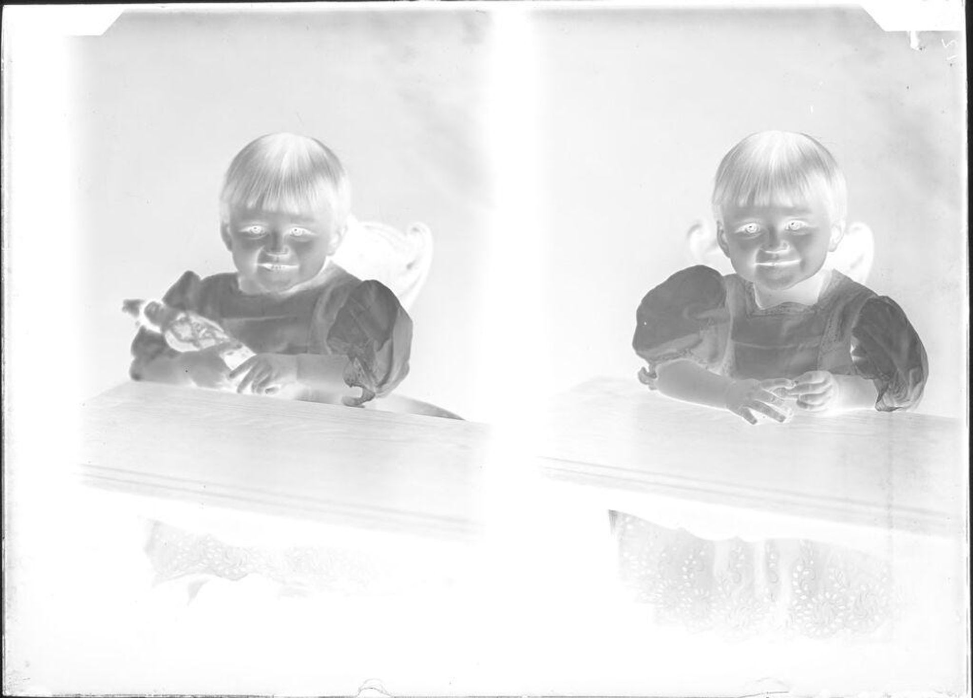 Untitled (two portraits of toddler seated at table, one carrying a doll) by John Deusing