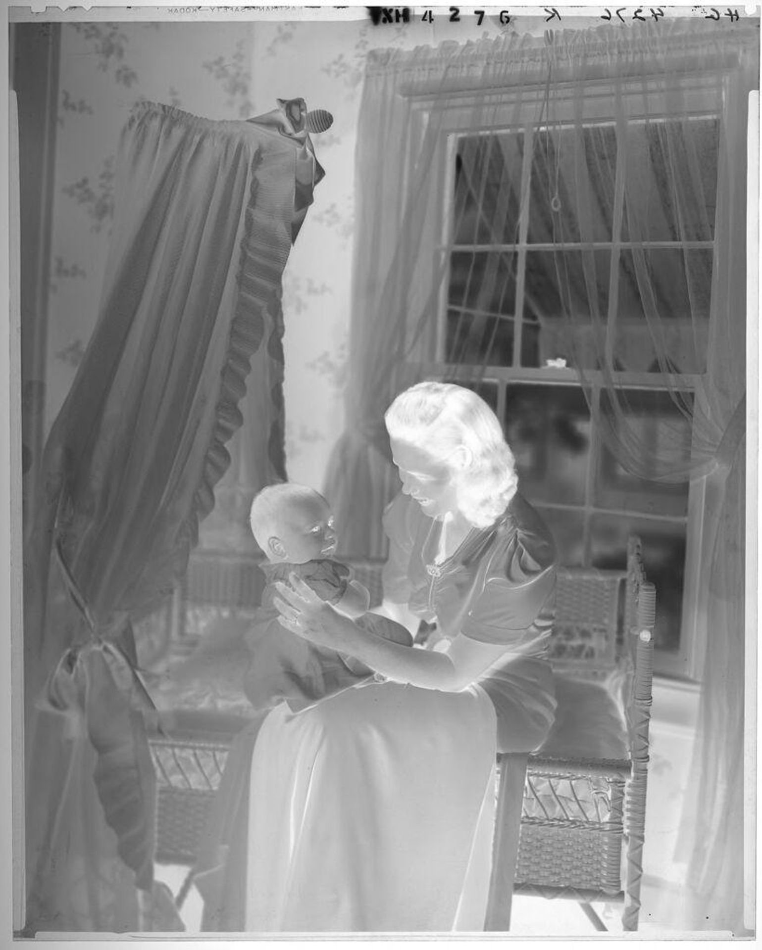 Untitled (woman seated at edge of bassinet looking at baby on lap) by Paul Gittings