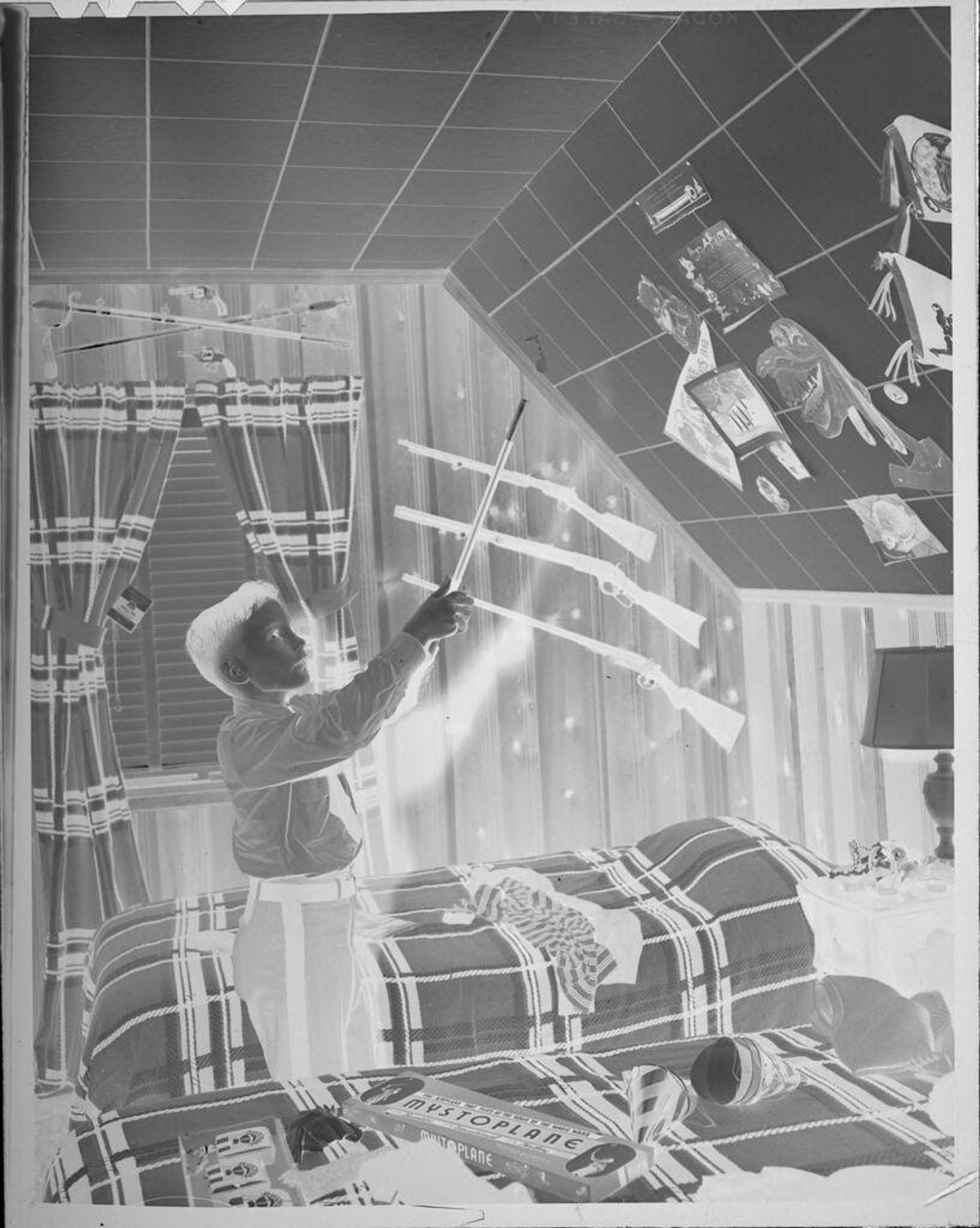Untitled (boy pointing at wall decorations in bedroom) by Lucian and Mary Brown