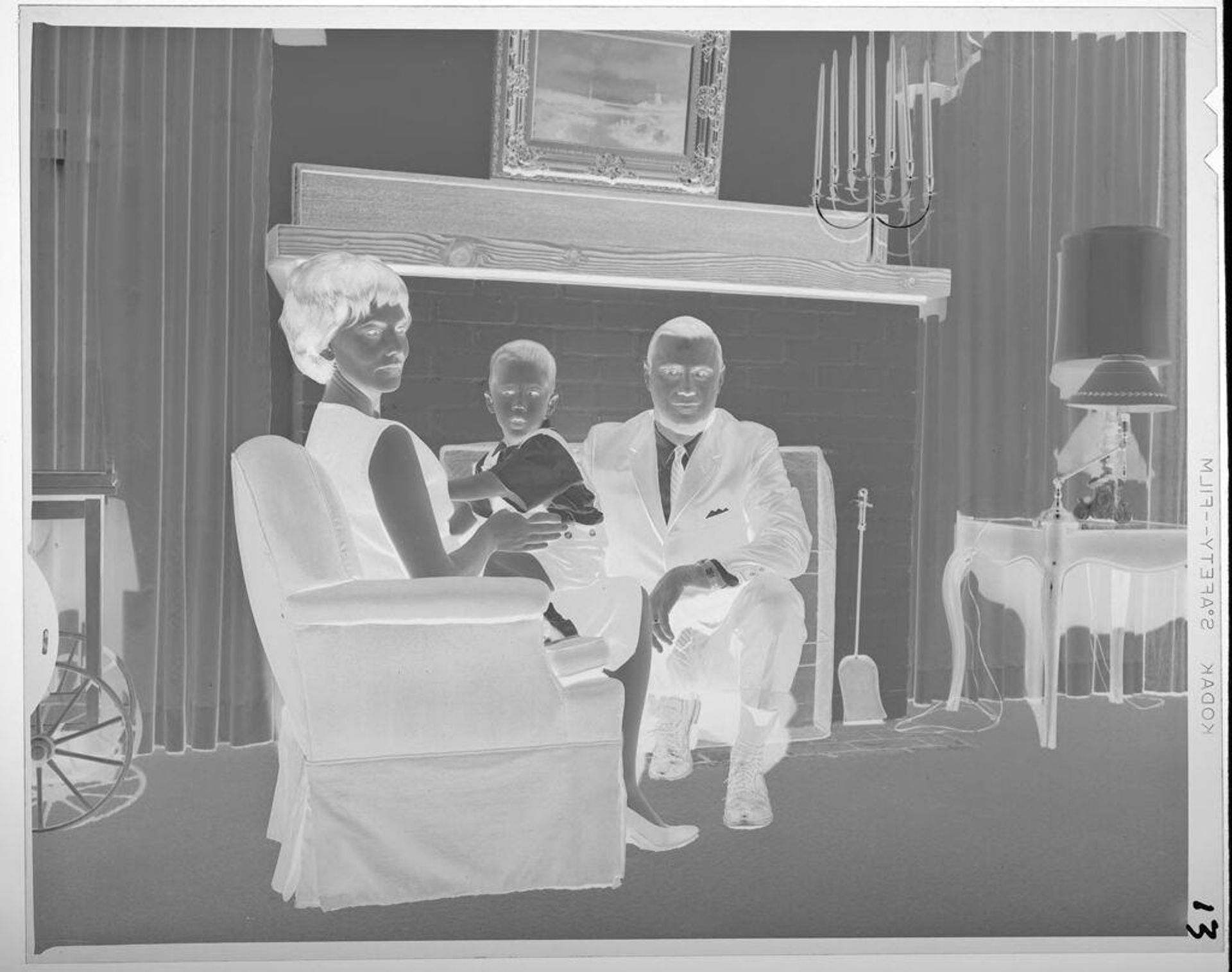 Untitled (man, woman, and baby, sitting in armchair in front of fireplace) by Jack Gould