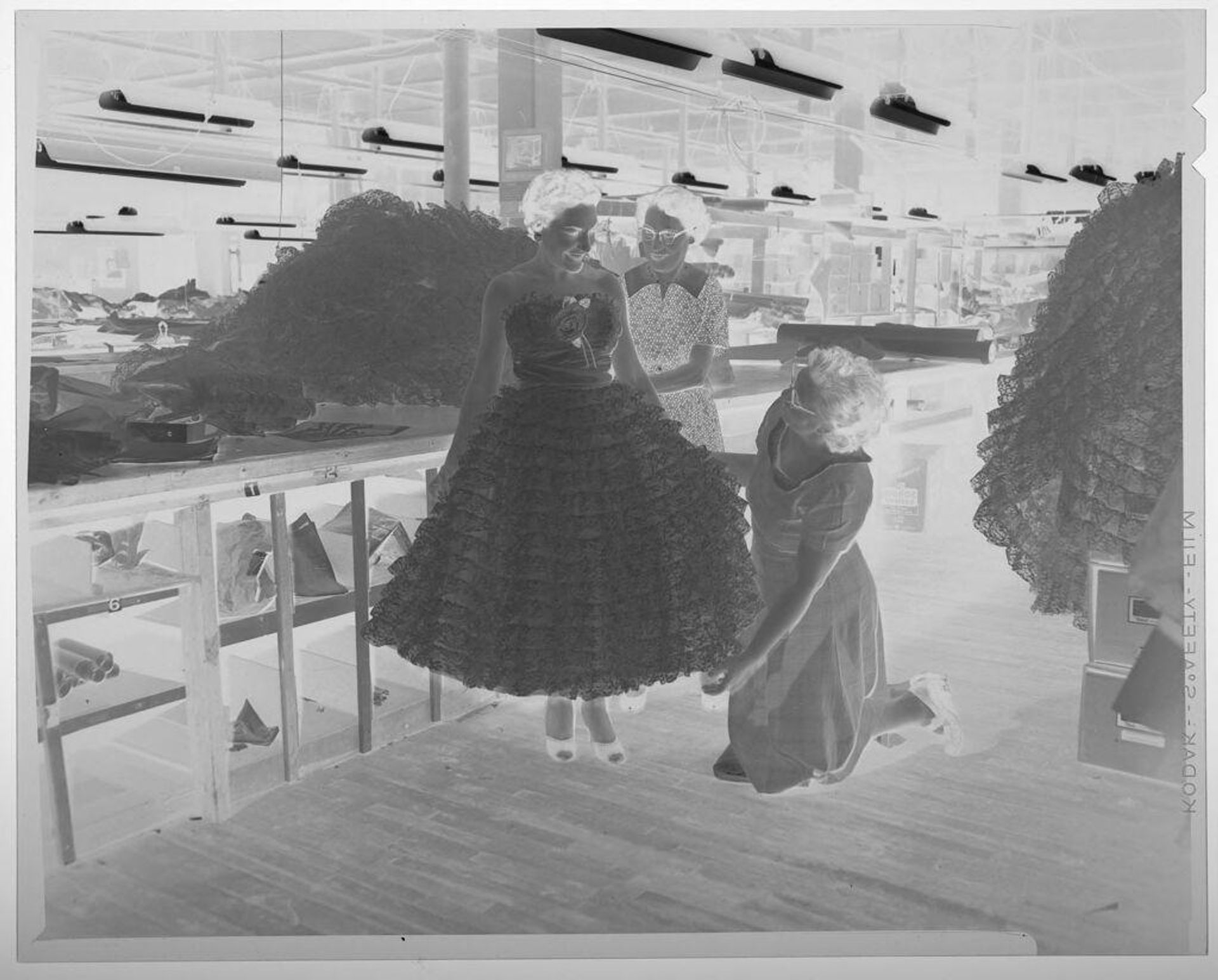 Untitled (two women inspecting dress of third woman inside large warehouse room) by Martin Schweig