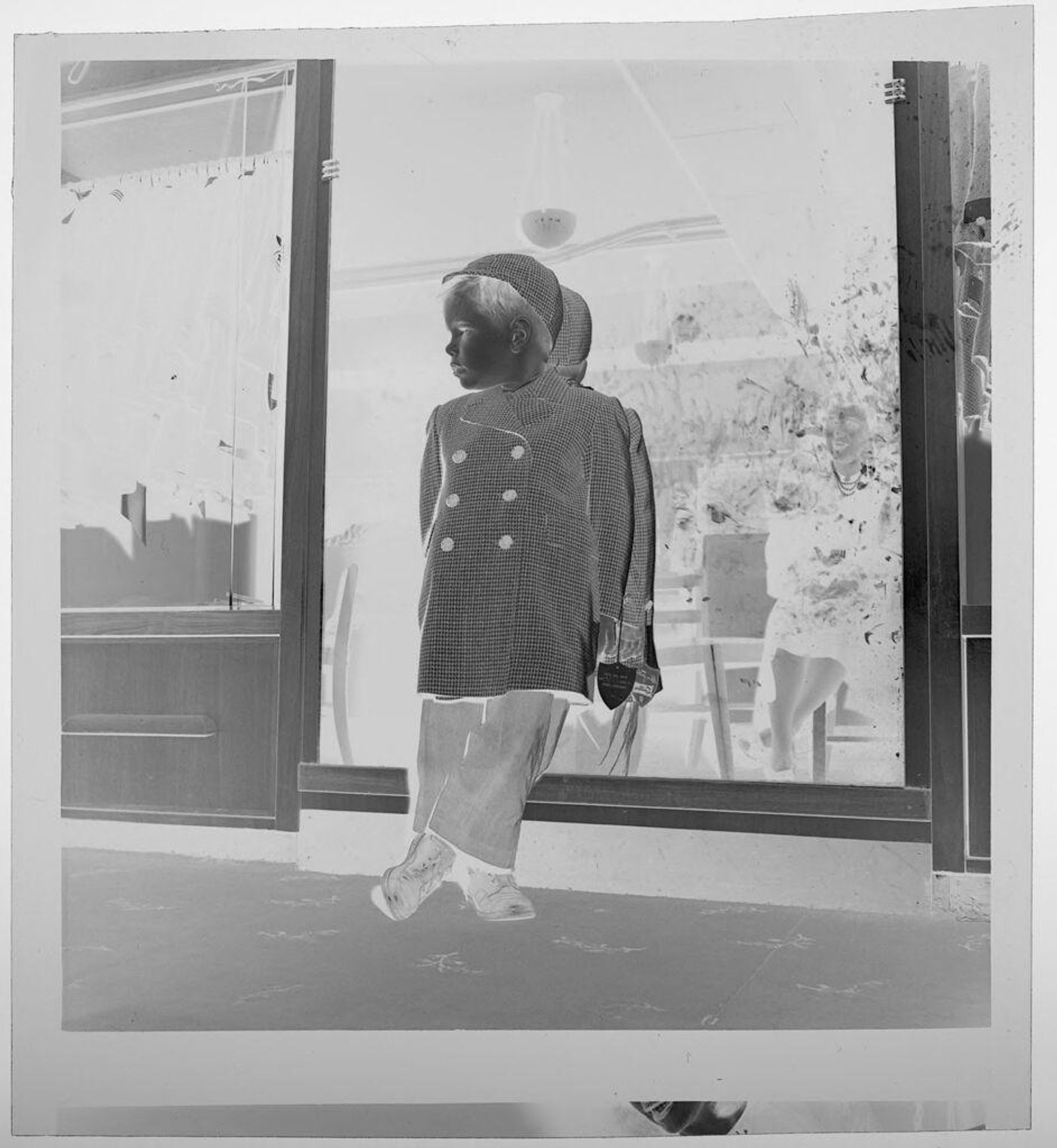 Untitled (child in hat and coat standing in front of shop window) by Jack Gould
