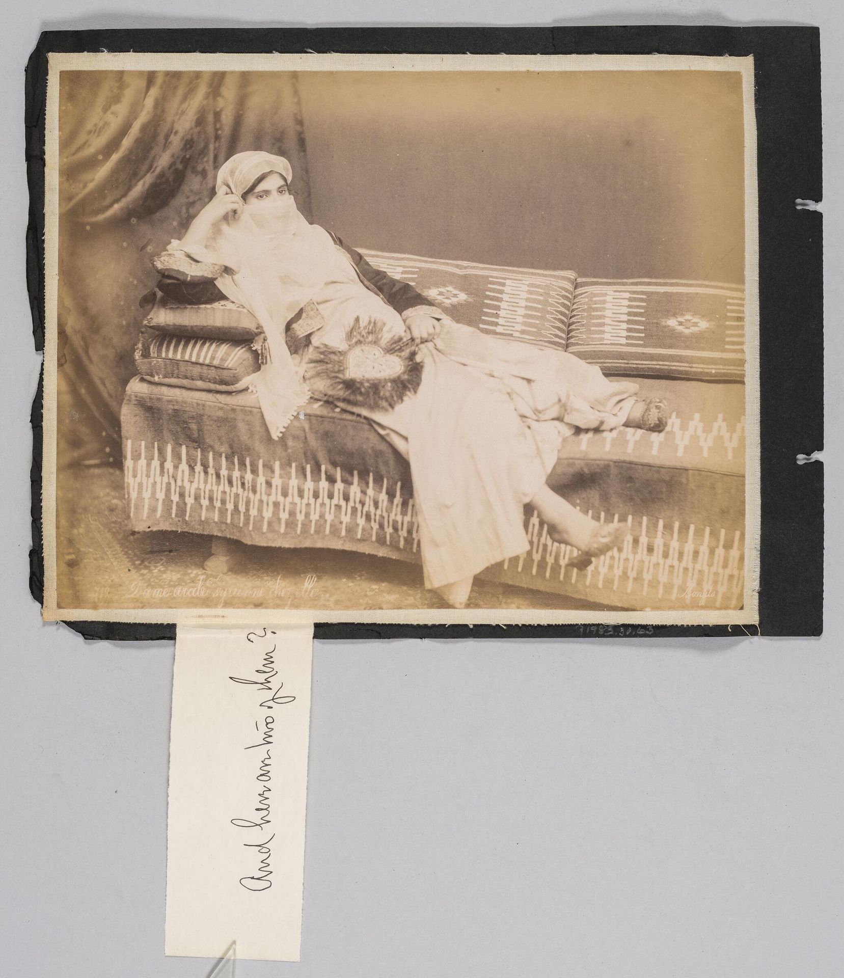 Untitled (woman in traditional dress, wearing a veil, holding a fan, reclining on a sofa) by Félix Bonfils