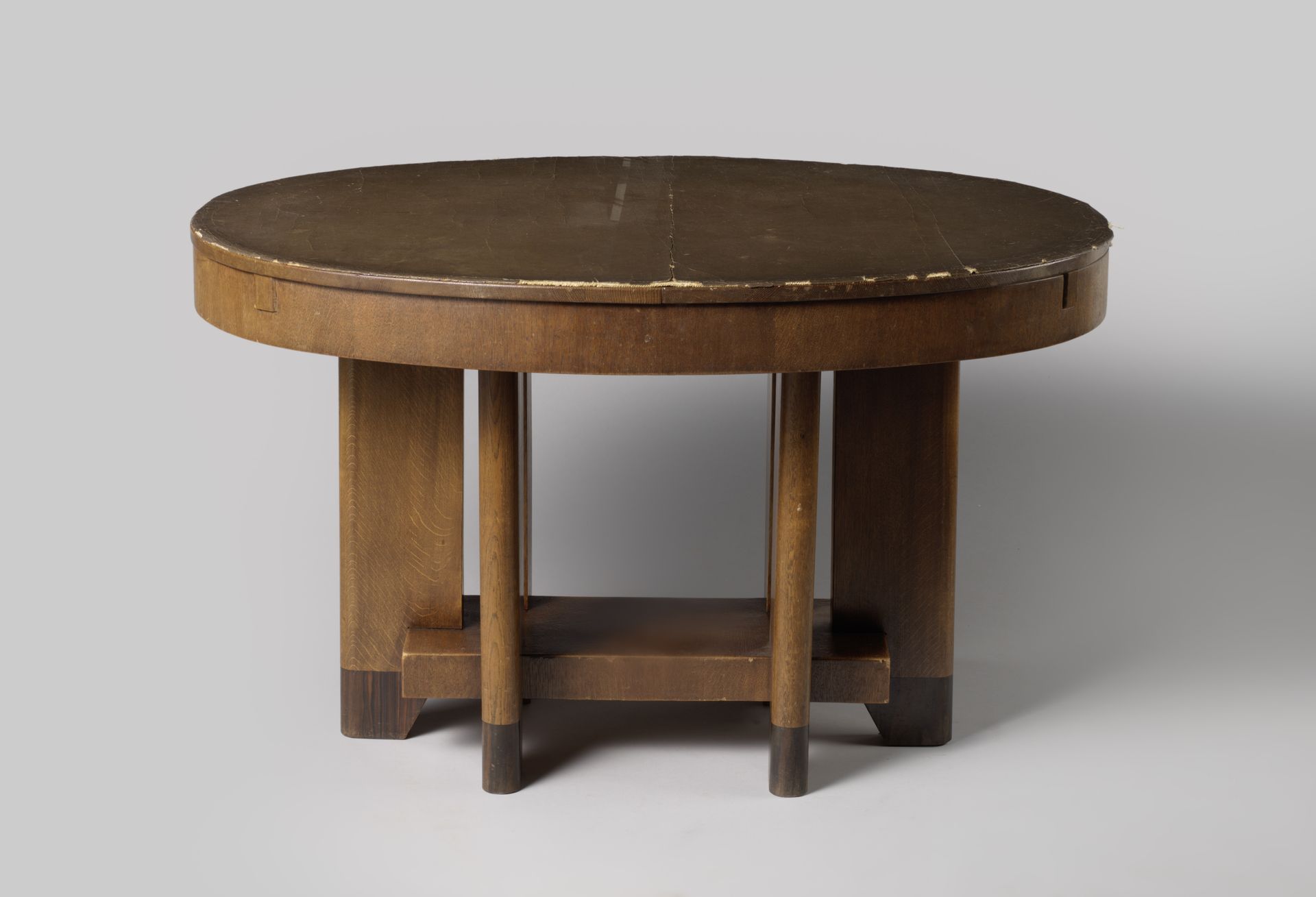 Tafel, ovaal, uitschuifbaar, op tweemaal drie brede platte poten, verbonden door een rechthoekig plateau. Bij de tafel horen twee uitschuifbladen by Klaas van den Berg