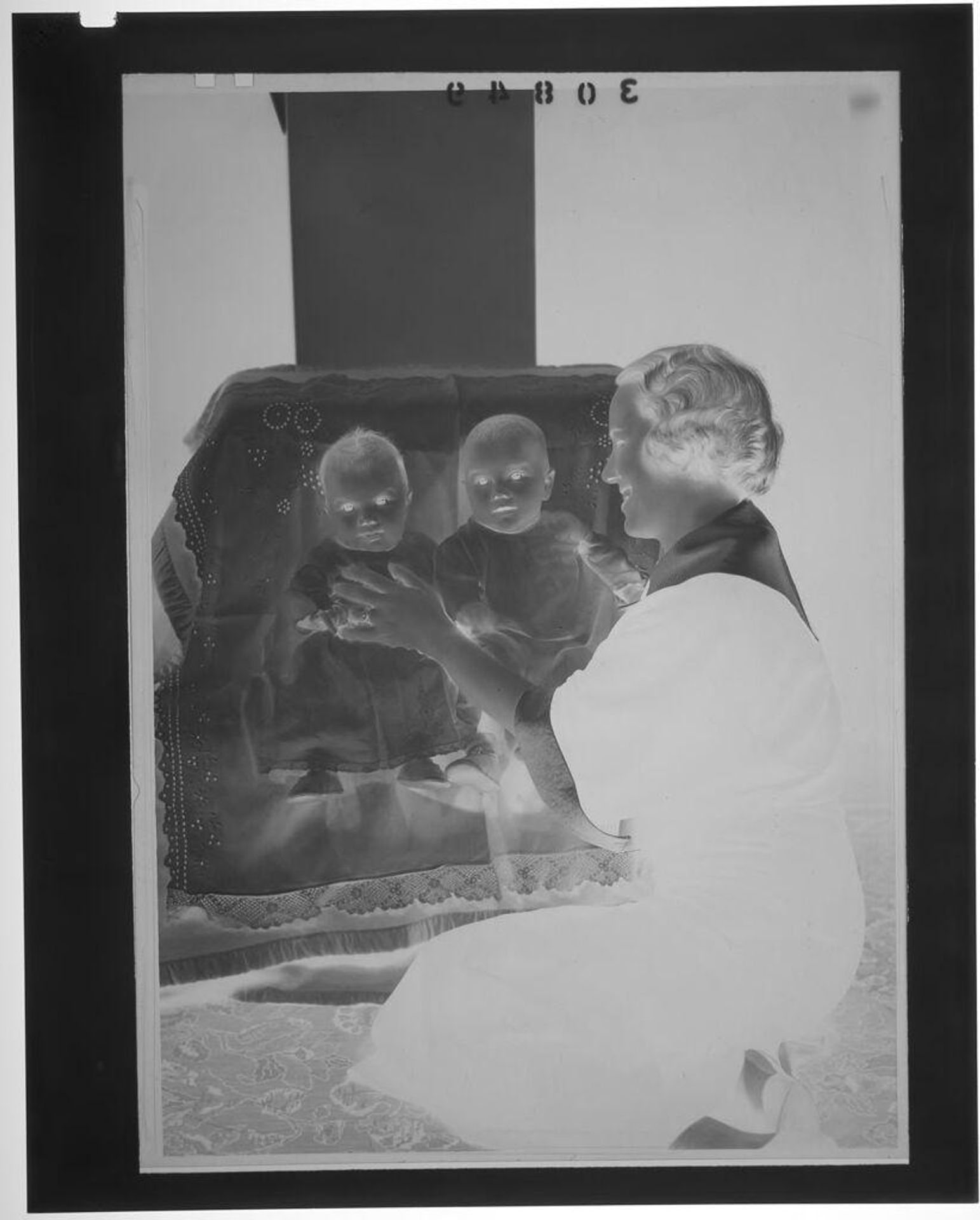 Untitled (woman smiling while standing over two babies in chair) by Martin Schweig