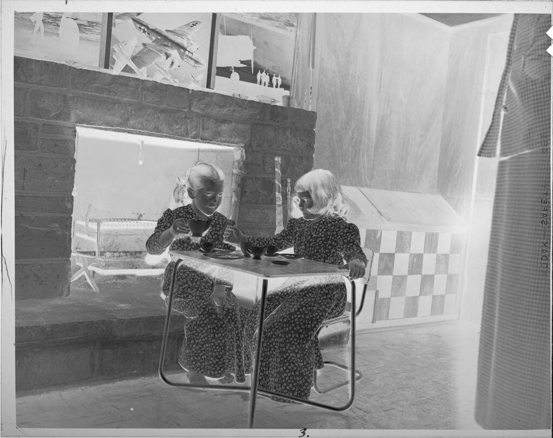 Untitled (two girls sitting at little table in front of fireplace) by Lucian and Mary Brown