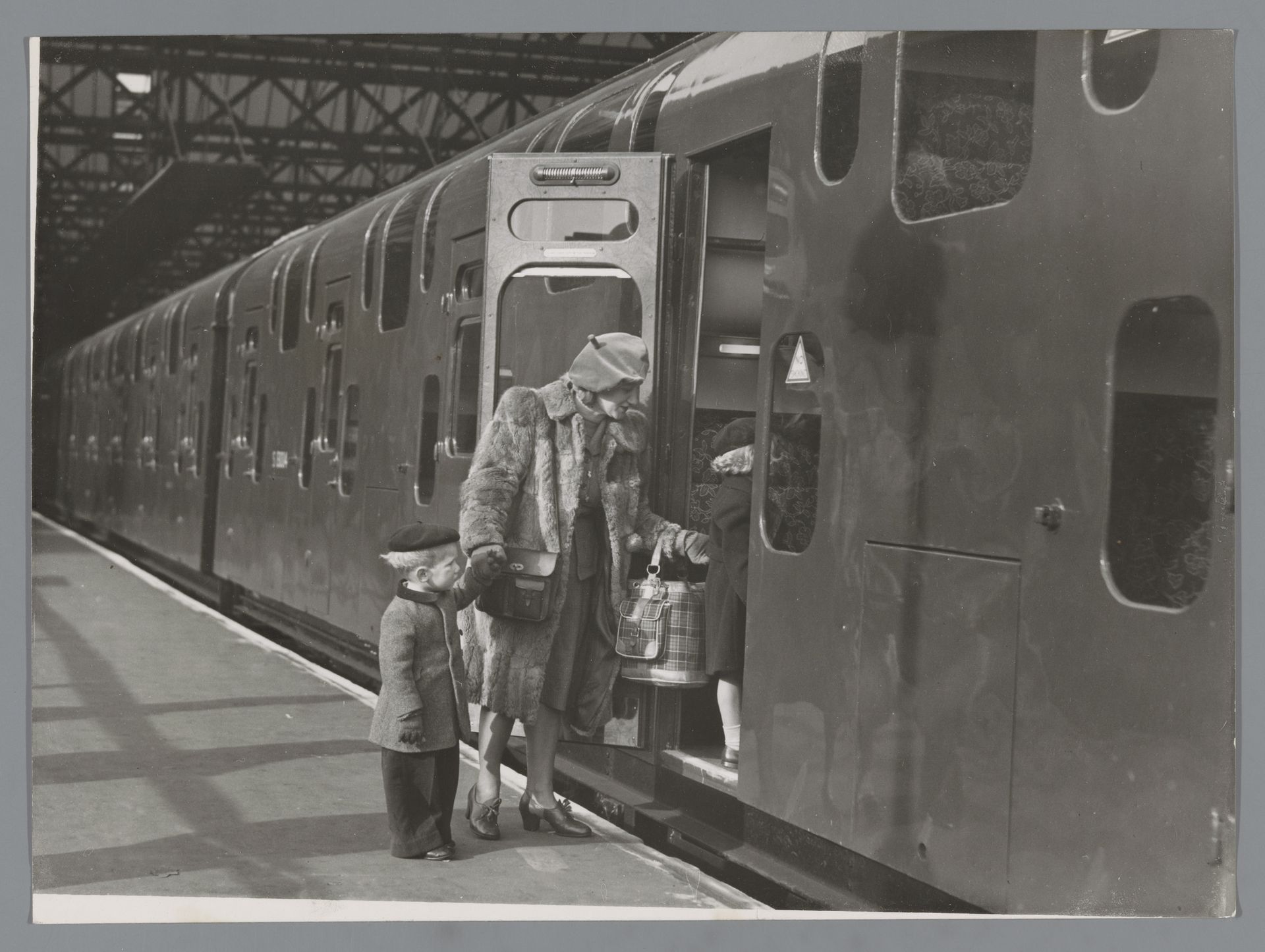 Vrouw en twee kinderen stappen in een dubbeldekkertrein op Charing Cross Station te Londen by R. Palmer