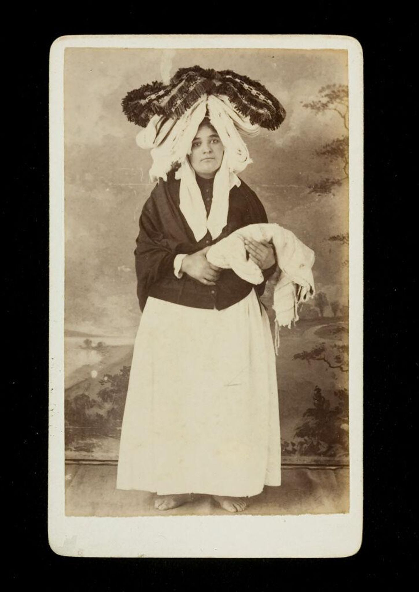 Costumes of Michaelenses, Azores, Portugal (barefoot woman standing, wearing dark shawl, large headdress, holding bundle of fabric(?)) by A.J. Rapozo