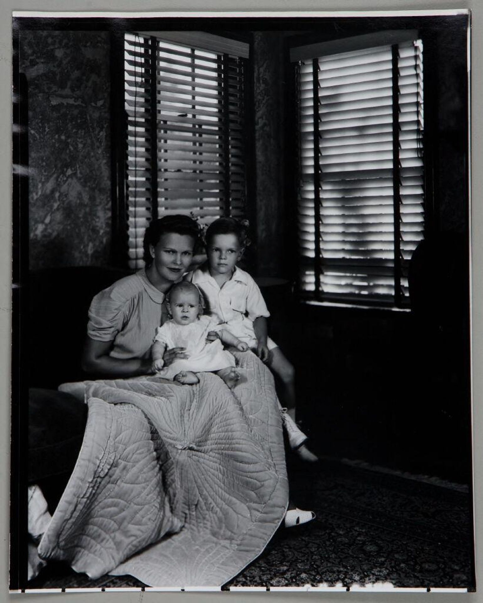 Untitled (woman seated on sofa with young boy and baby, quilt spread out over lap) by Paul Gittings