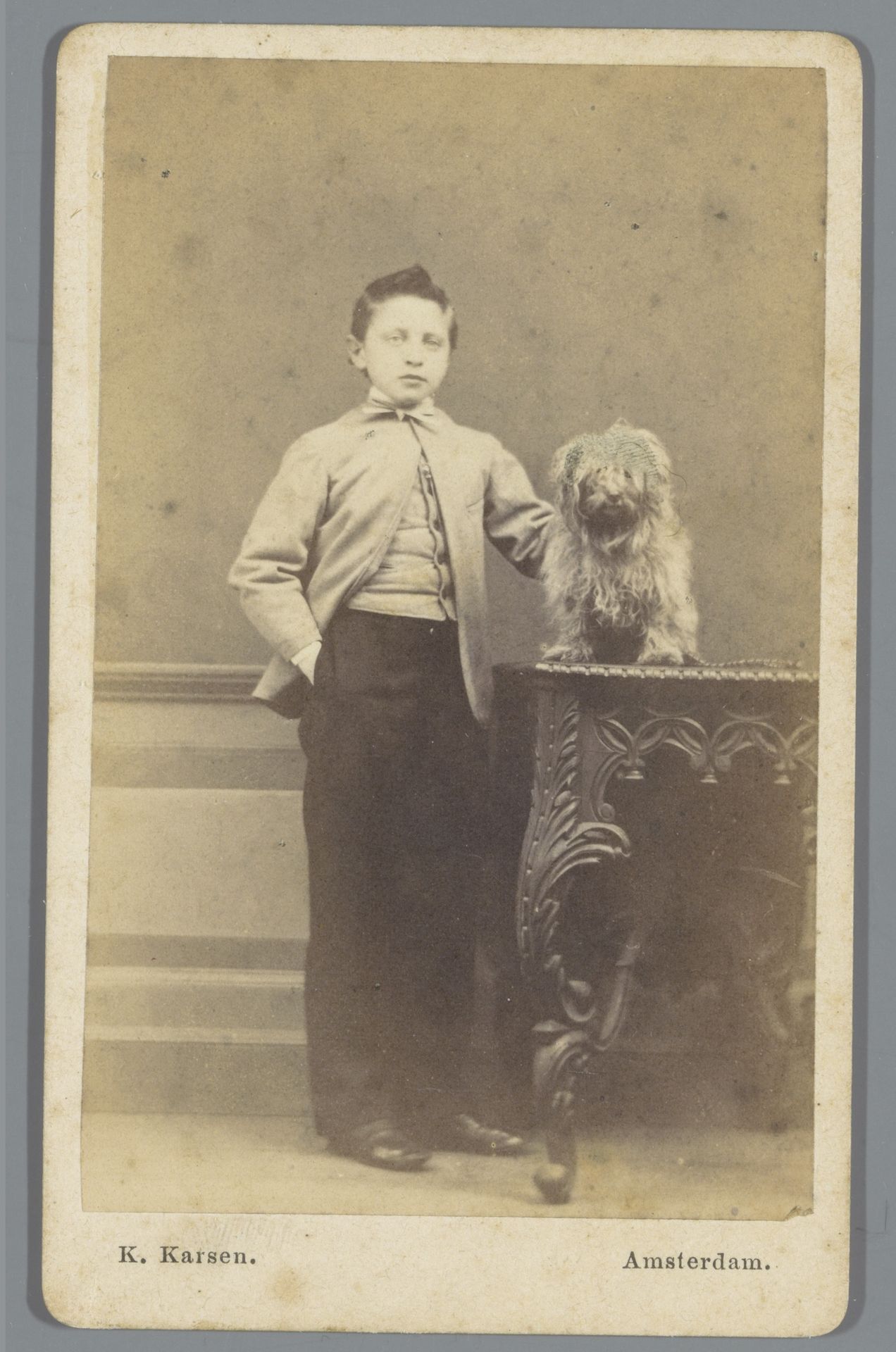 Portret van een onbekende jongen, staande naast een tafel waarop een hond zit by Kasparus Karsen
