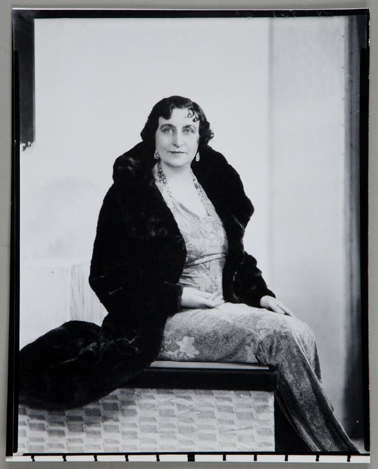 Untitled (woman in long fur coat, earrings, necklace and long dress seated in studio) by Paul Gittings
