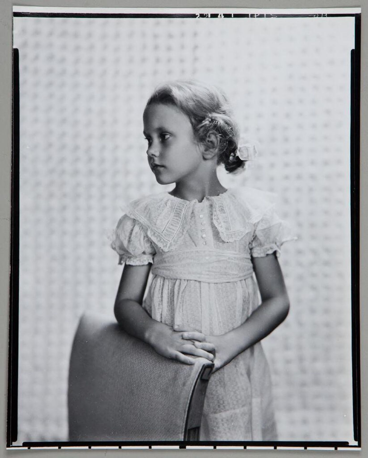 Untitled (portrait of blond girl with bow in hair standing behind chair, looking left) by Paul Gittings