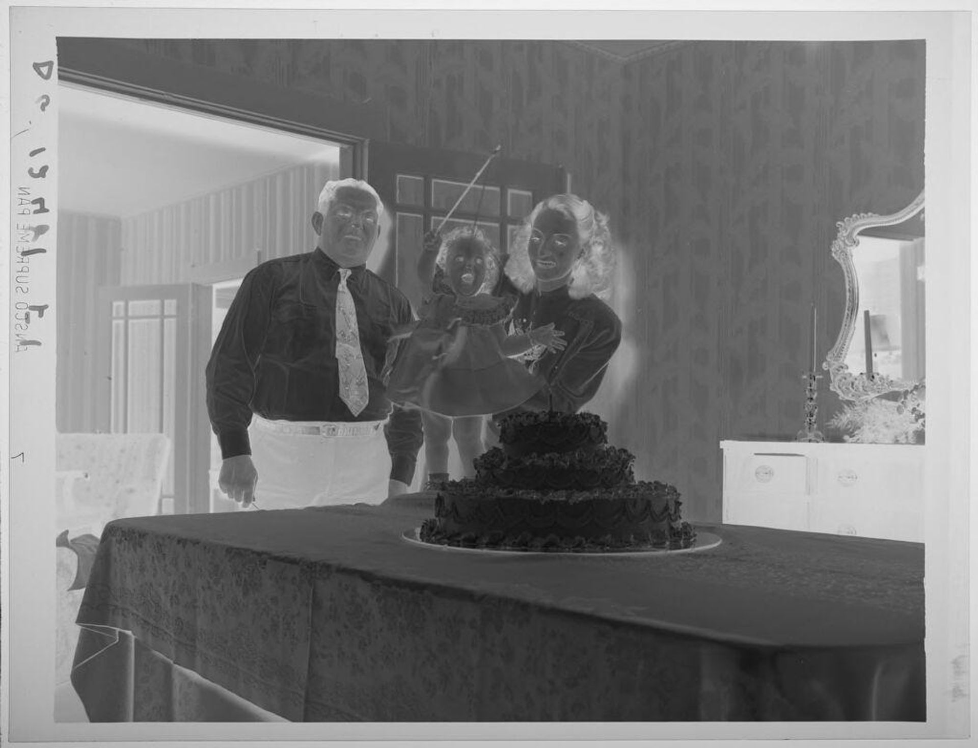 Untitled (little girl standing on table by three-tiered first birthday cake with parents at her side) by Paul Gittings