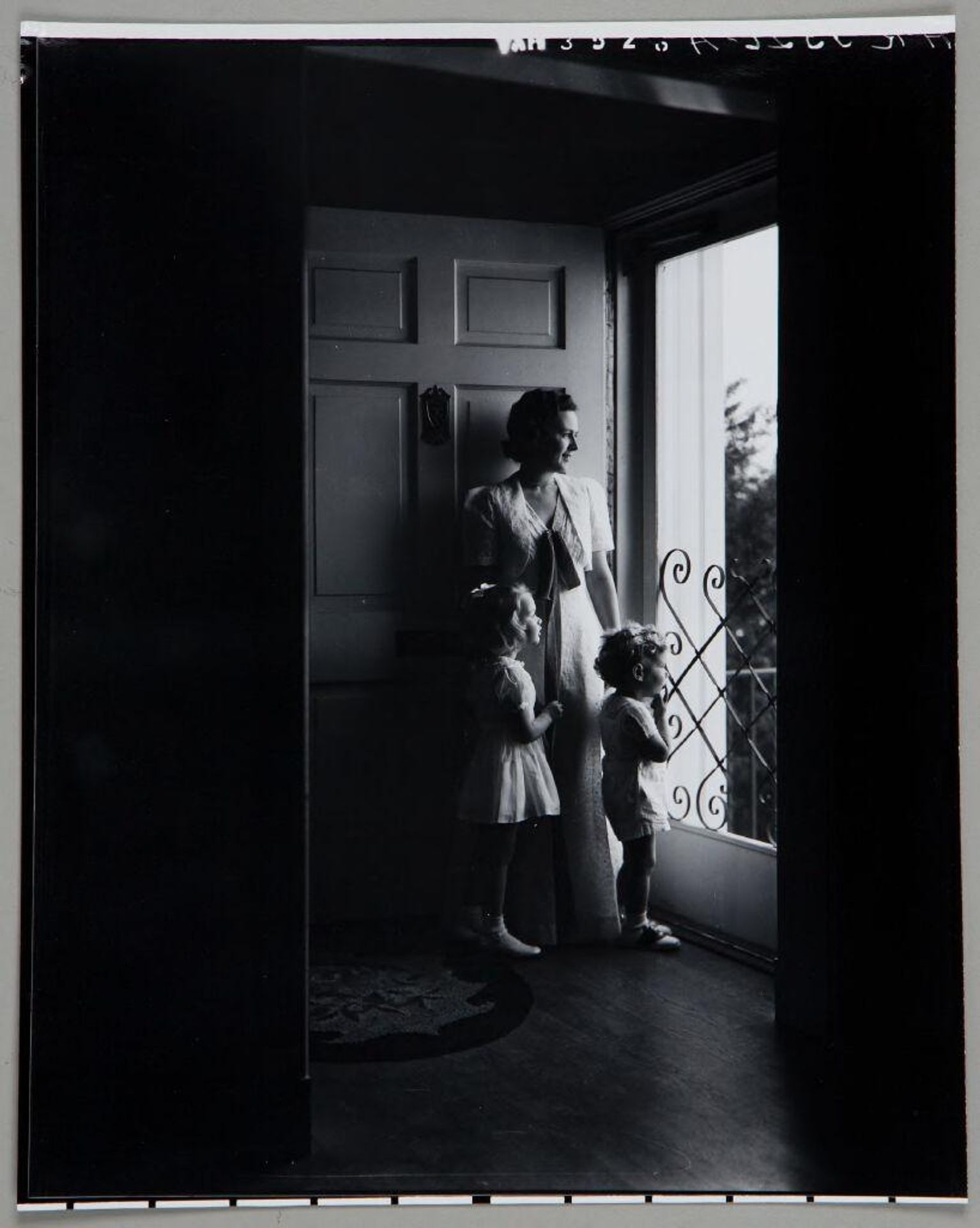 Untitled (woman standing with young son and daughter in doorway, looking out screen door) by Paul Gittings