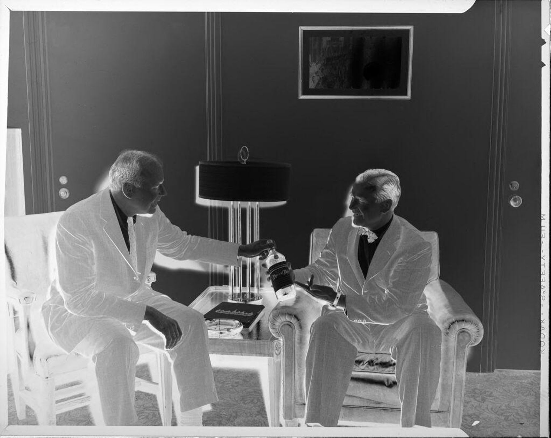 Untitled (two men sitting, holding bottle) by Peter James Studio