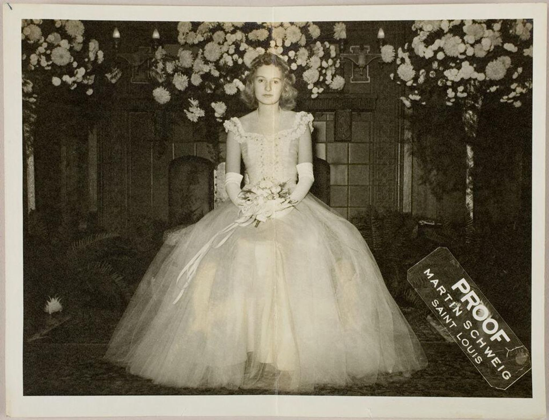 Untitled (bride with straight face posed seated in front of fireplace with flowers on top) by Martin Schweig