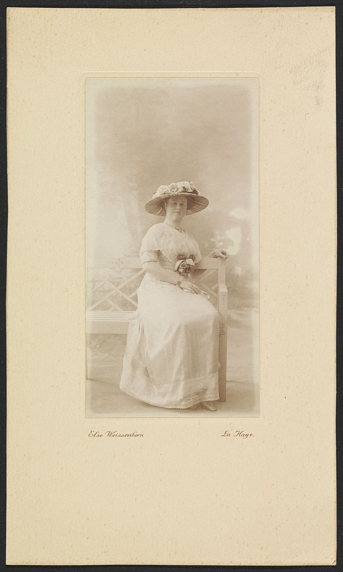 Portret van mevrouw M.C. Lucassen-Van Idsinga met hoed en jurk zittend op een bank by Else Weissenborn