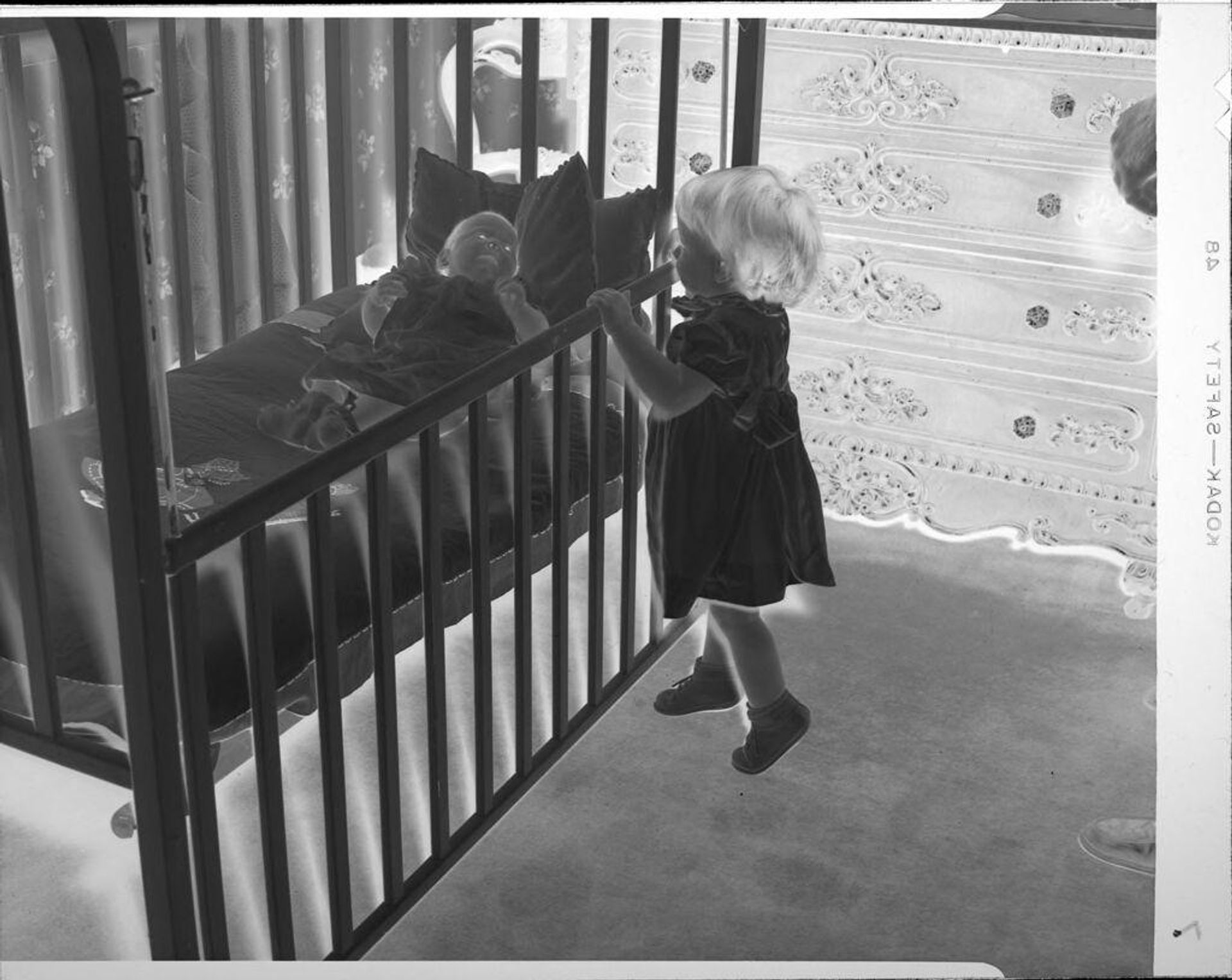 Untitled (child looking at baby in crib) by John Howell