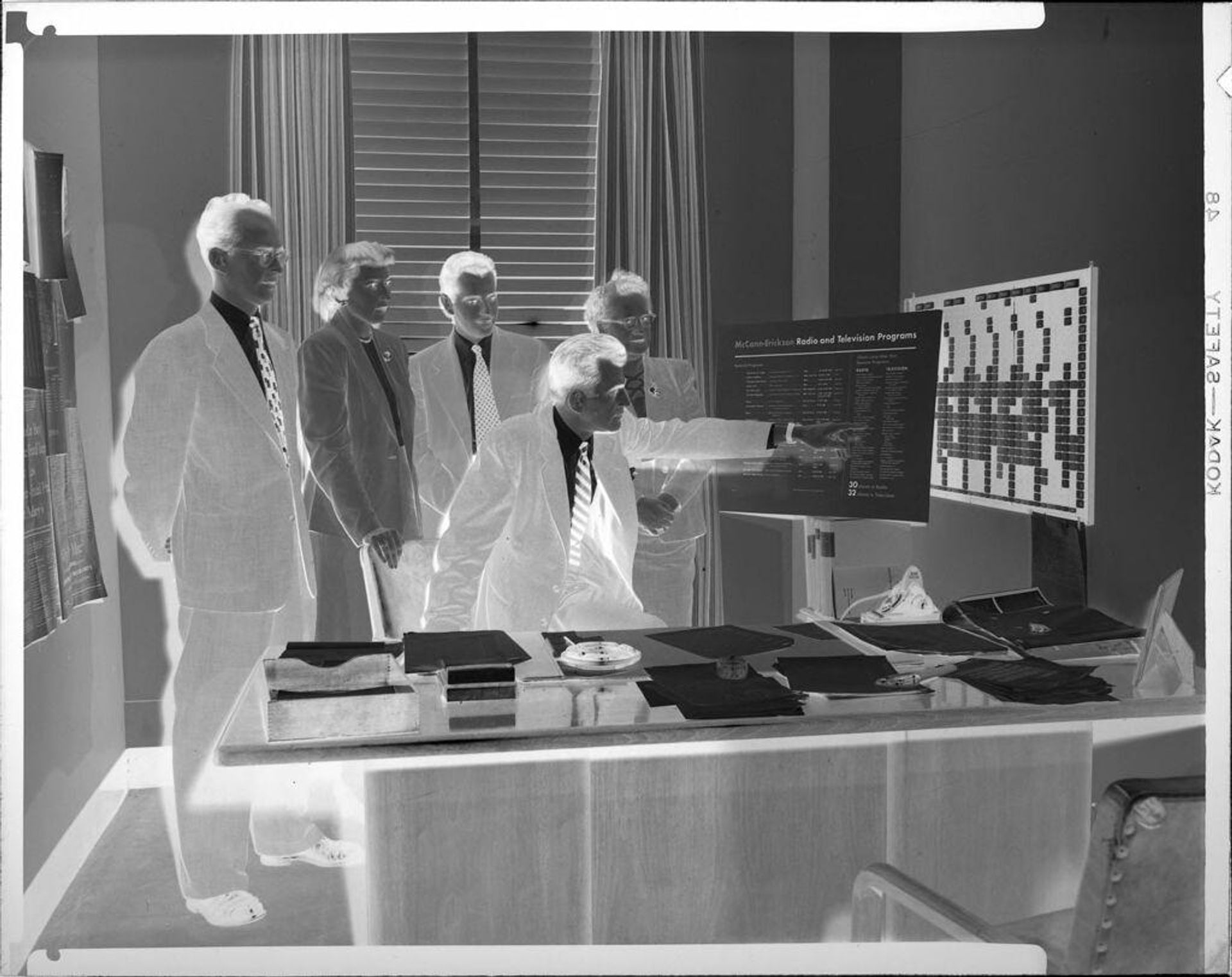 Untitled (advertising executives behind desk looking at charts) by Peter James Studio