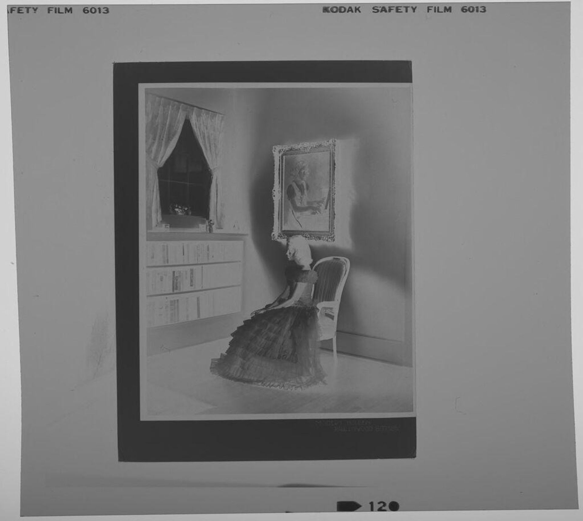 Untitled (photograph of girl in formal dress seated by bookshelves, under painting of girl playing piano) by Paul Gittings