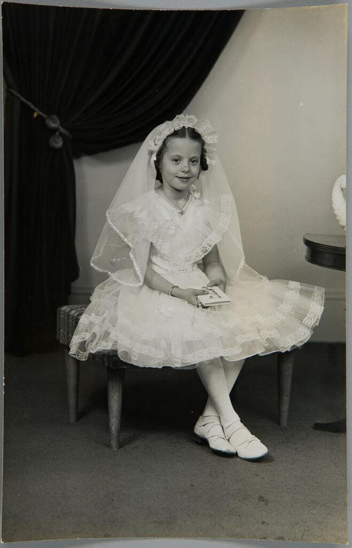 Untitled (girl seated in white dress and veil, holding religious book) by John Deusing