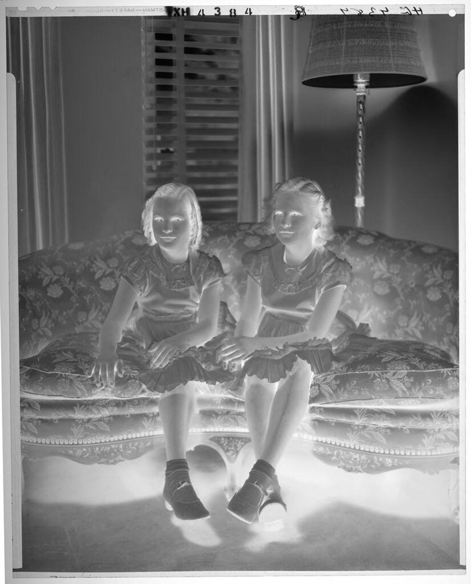 Untitled (two girls in matching dresses seated on floral sofa) by Paul Gittings