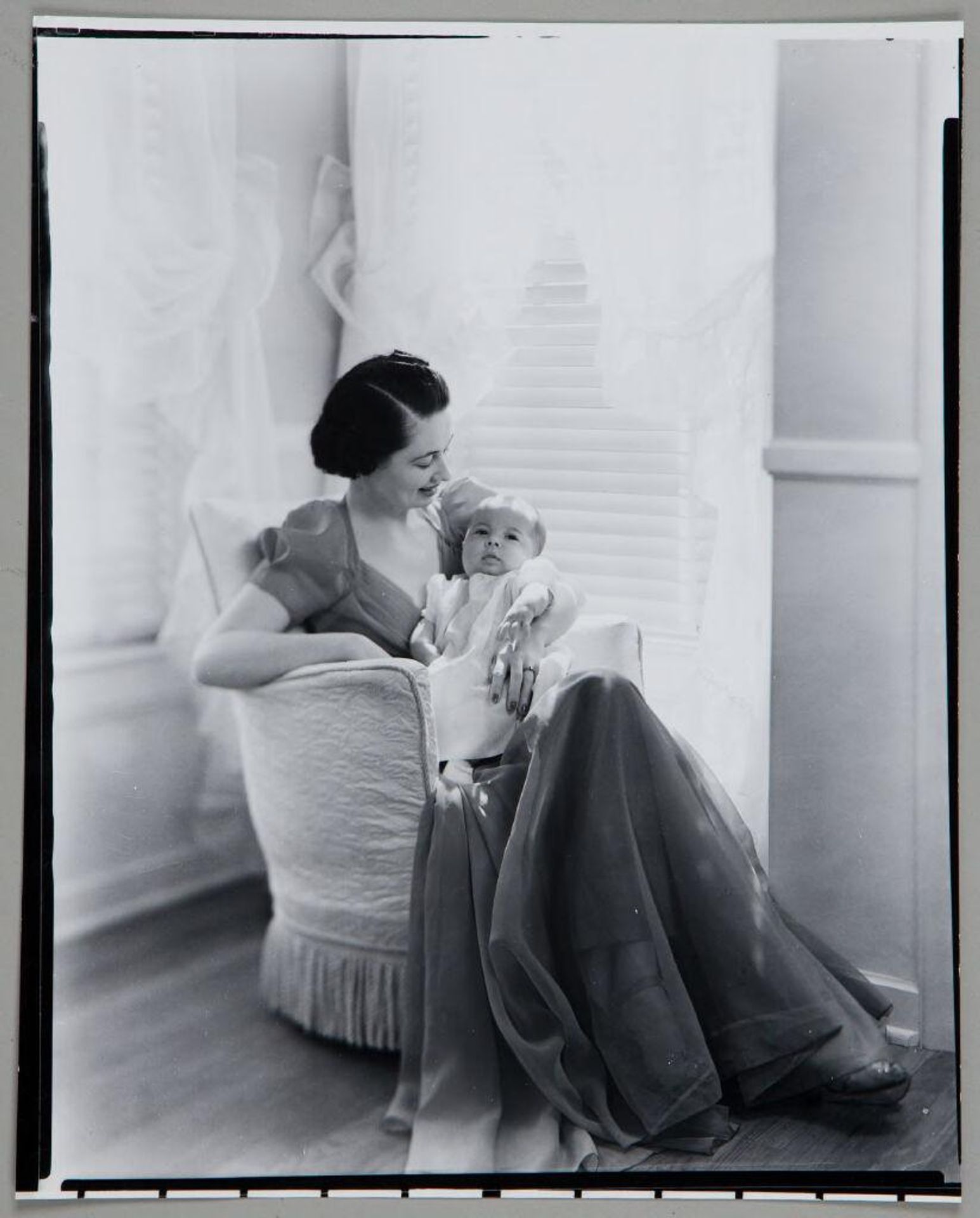 Untitled (woman seated on upholstered chair with baby, in front of windows) by Paul Gittings