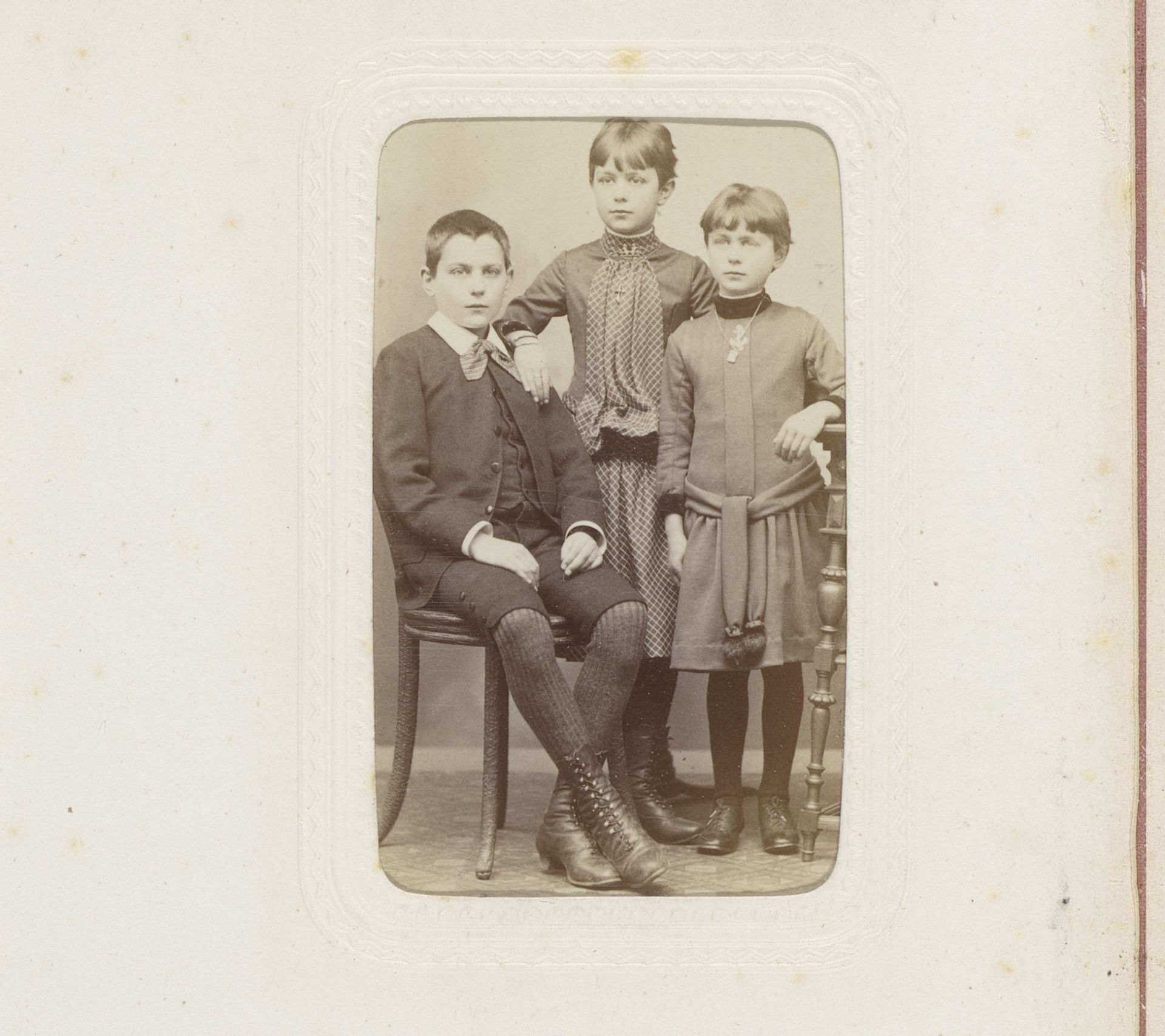 Portret van drie kinderen, waarvan één zittend op een stoel by Wolffram & Comp.