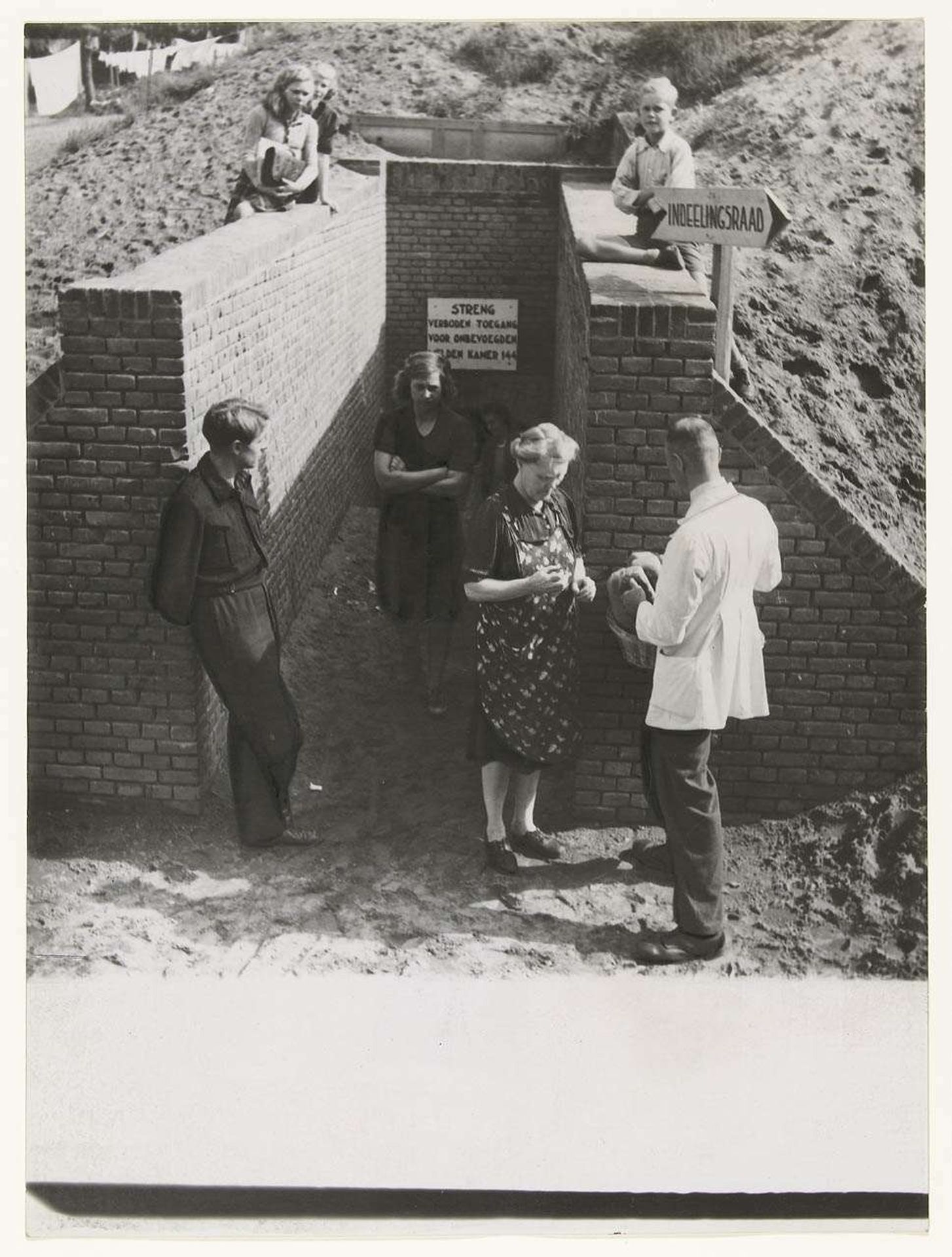 Mannen, vrouwen en kinderen bij de ingang van een schuilkelder in Nijmegen by Associated Correspondents