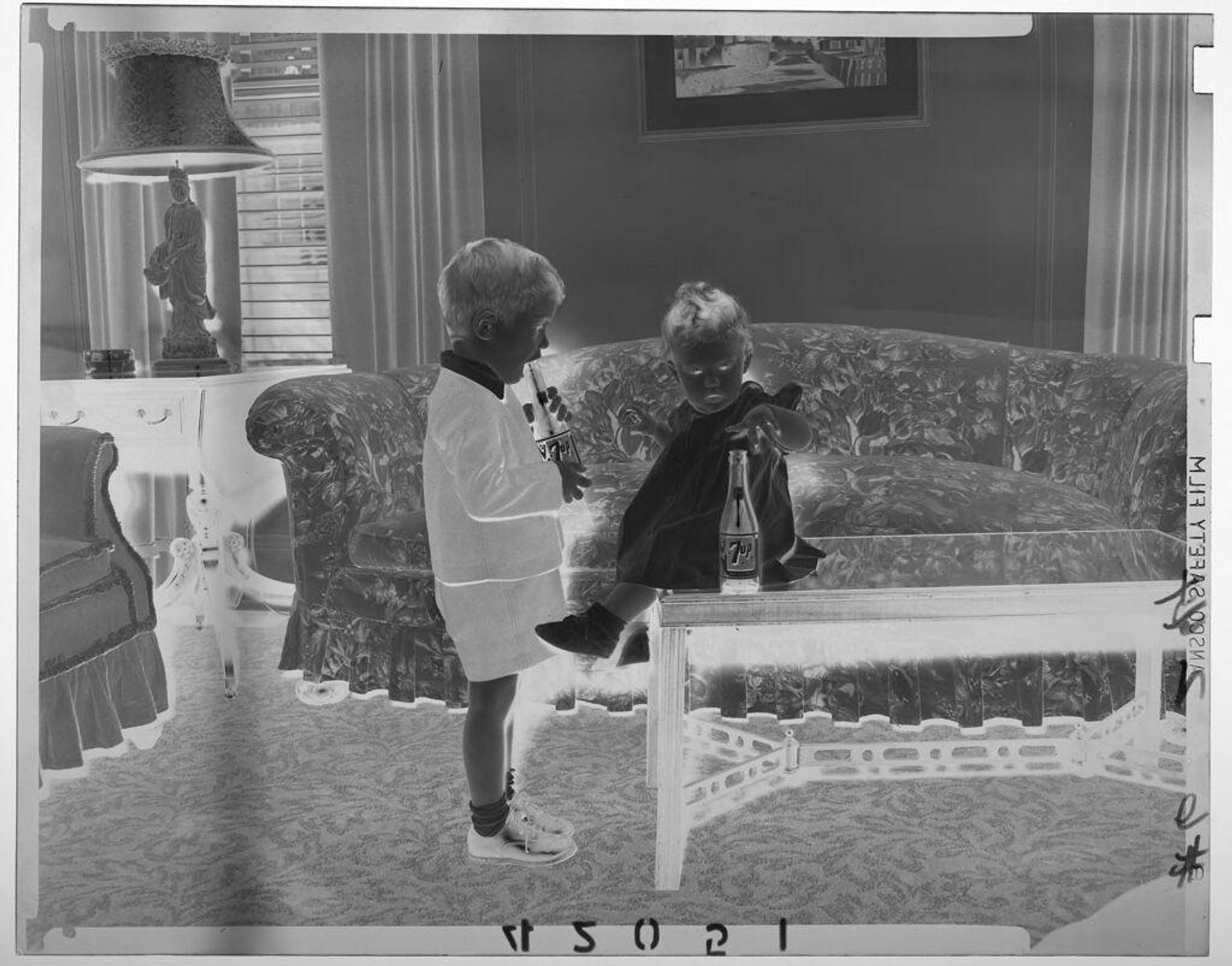 Untitled (young boy and baby girl playing with 7-Up bottles in living room) by Martin Schweig