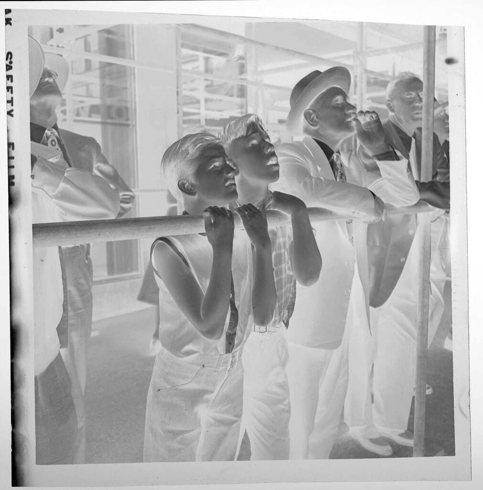 Untitled (two boys and men leaning on bar and looking up) by Jack Gould