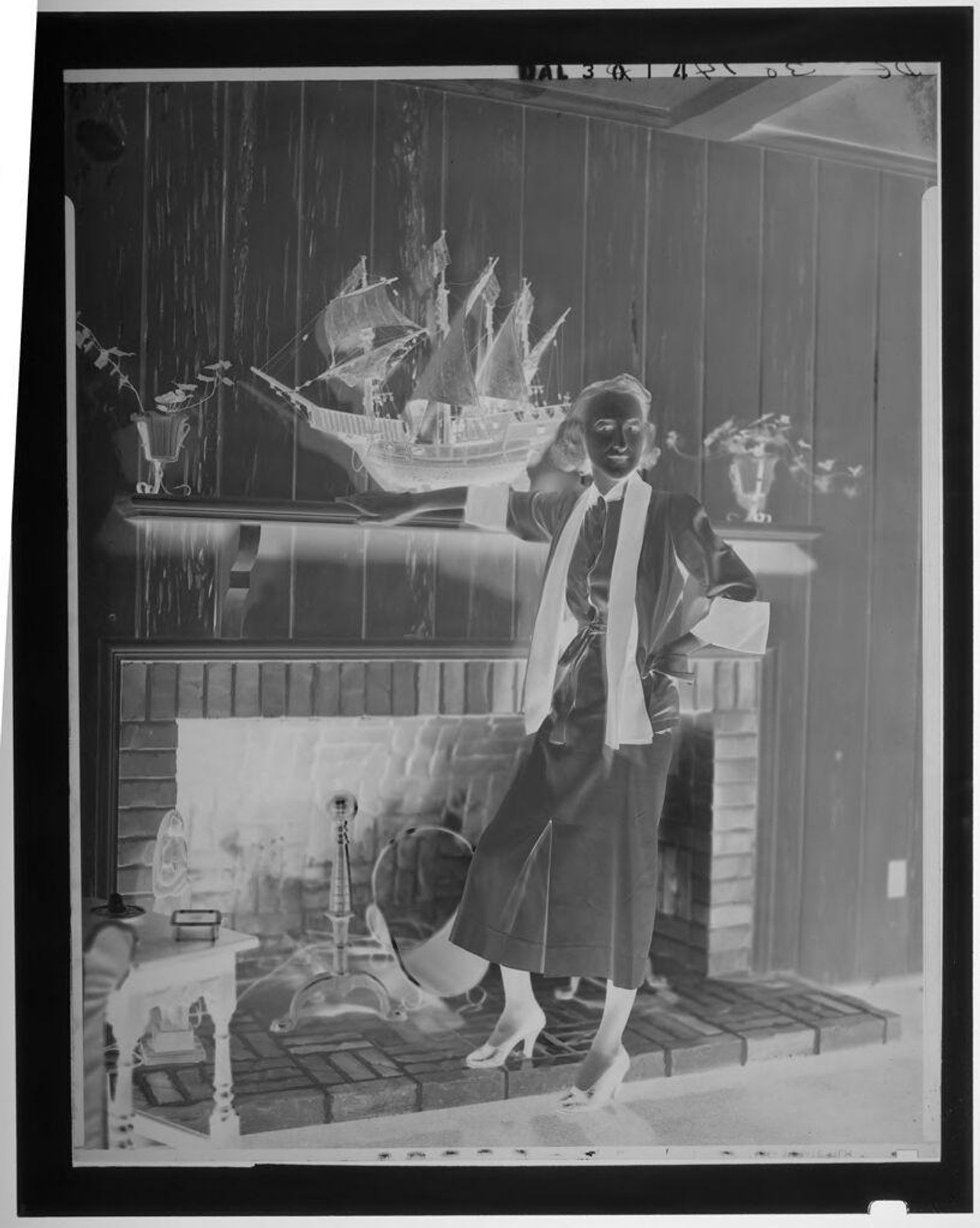 Untitled (woman standing next to fireplace with model ship on mantel) by Paul Gittings